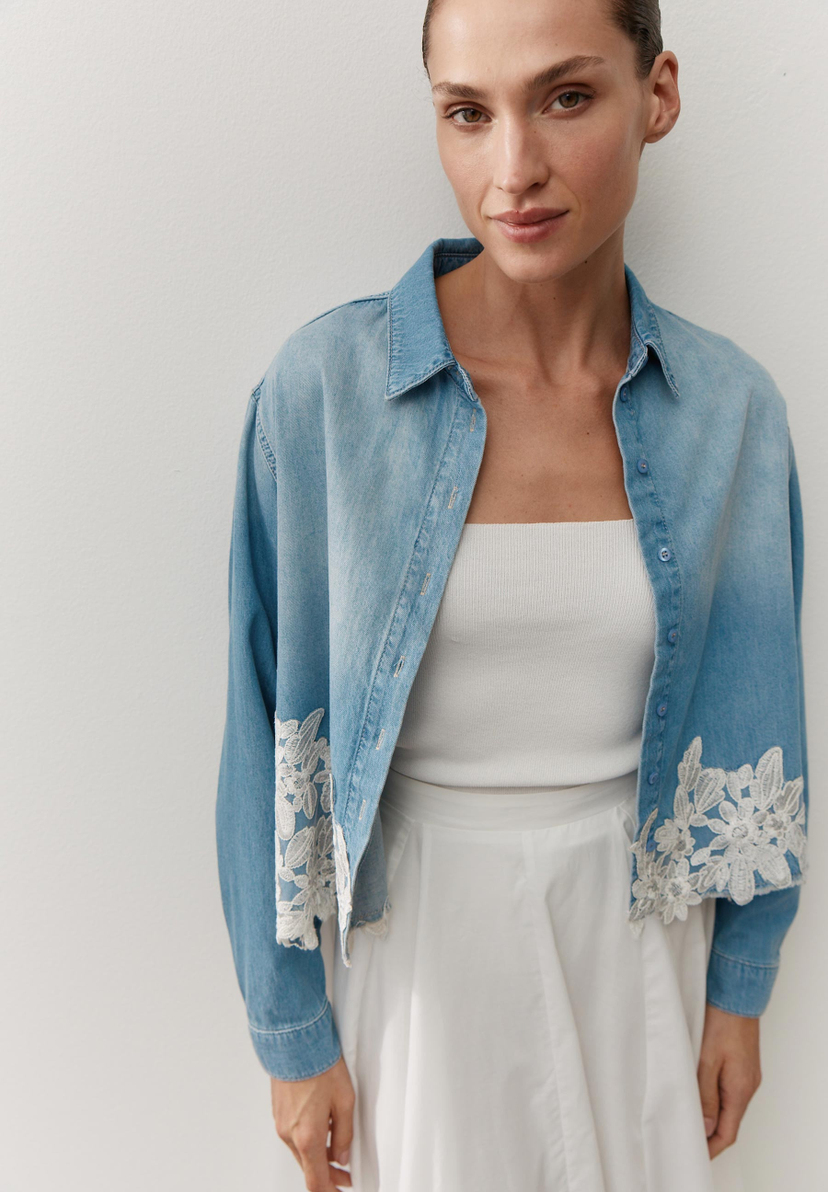 Eine Frau trägt eine helle Jeansbluse von MORE & MORE mit weißer Spitze am Saum. Eine Frau trägt eine helle Jeansbluse von MORE & MORE mit weißer Spitze am Saum.