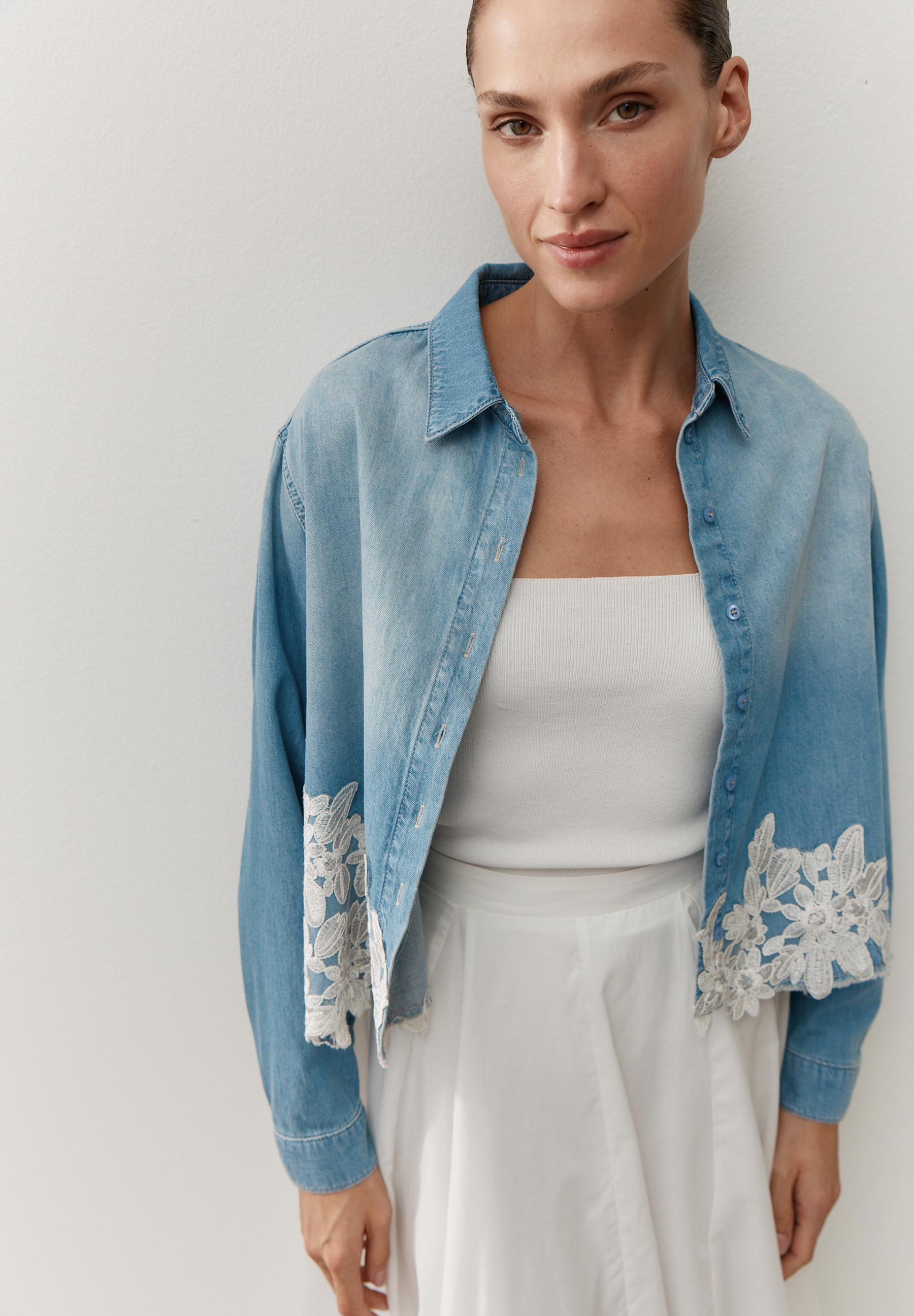 Eine Frau trägt eine helle Jeansbluse von MORE & MORE mit weißer Spitze am Saum.