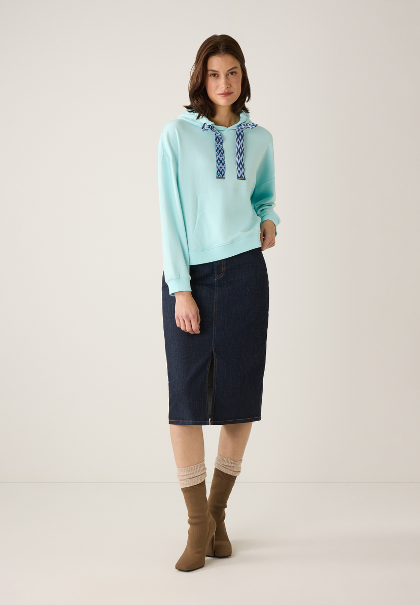 Eine Frau in einem MORE & MORE Sweatshirt mit Kapuze in Hellblau und einem Jeansrock. Eine Frau in einem MORE & MORE Sweatshirt mit Kapuze in Hellblau und einem Jeansrock.