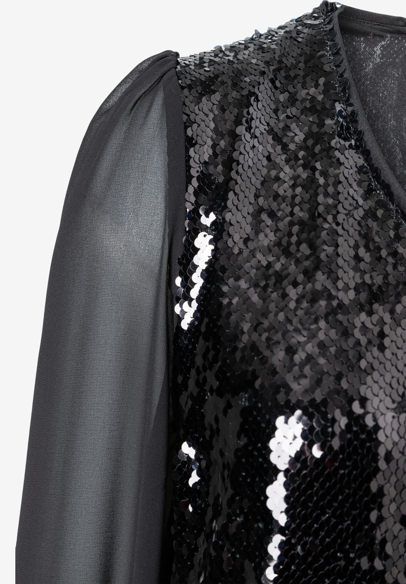 Detailaufnahme von MORE & MORE Oberteil, schwarze Pailletten und transparente Ärmel. Detailaufnahme von MORE & MORE Oberteil, schwarze Pailletten und transparente Ärmel.