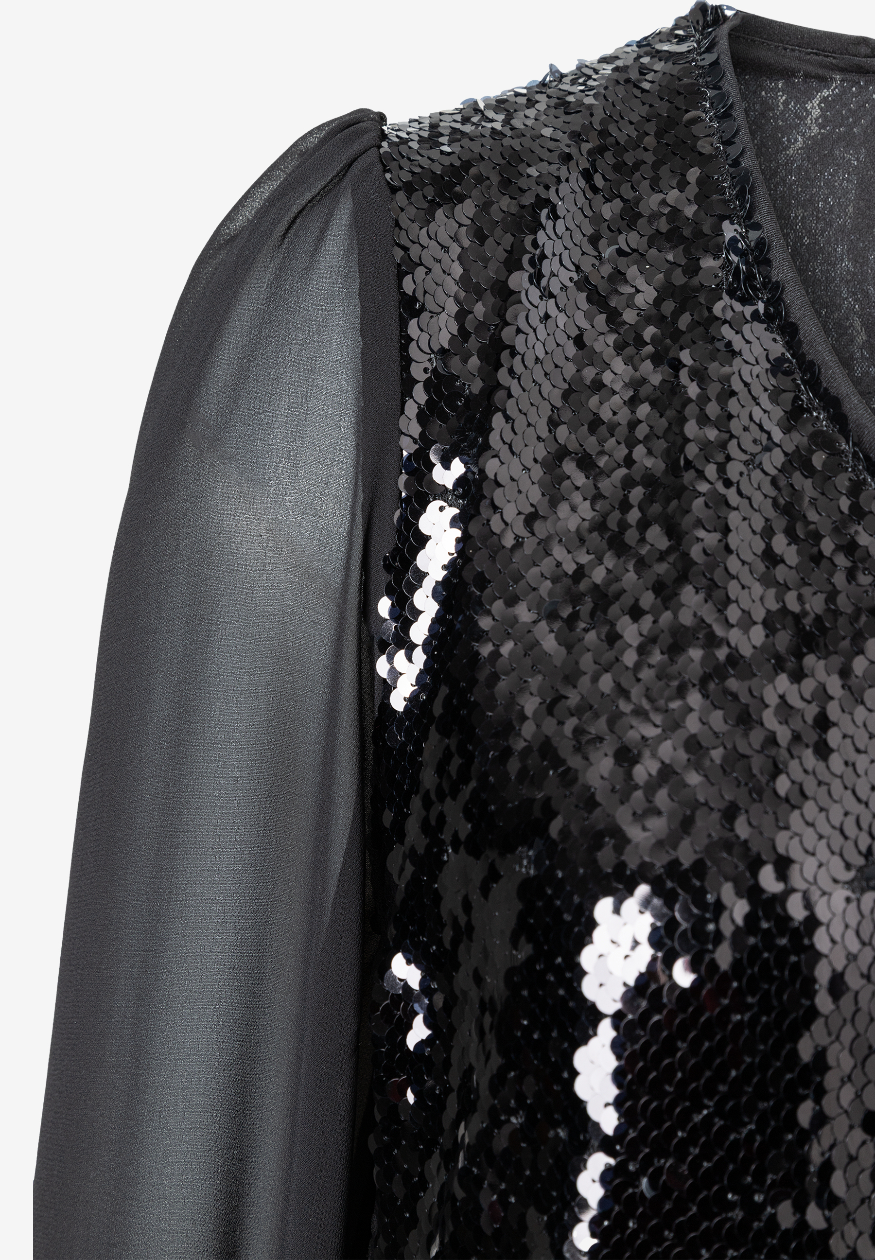 Detailaufnahme von MORE & MORE Oberteil, schwarze Pailletten und transparente Ärmel. Detailaufnahme von MORE & MORE Oberteil, schwarze Pailletten und transparente Ärmel.