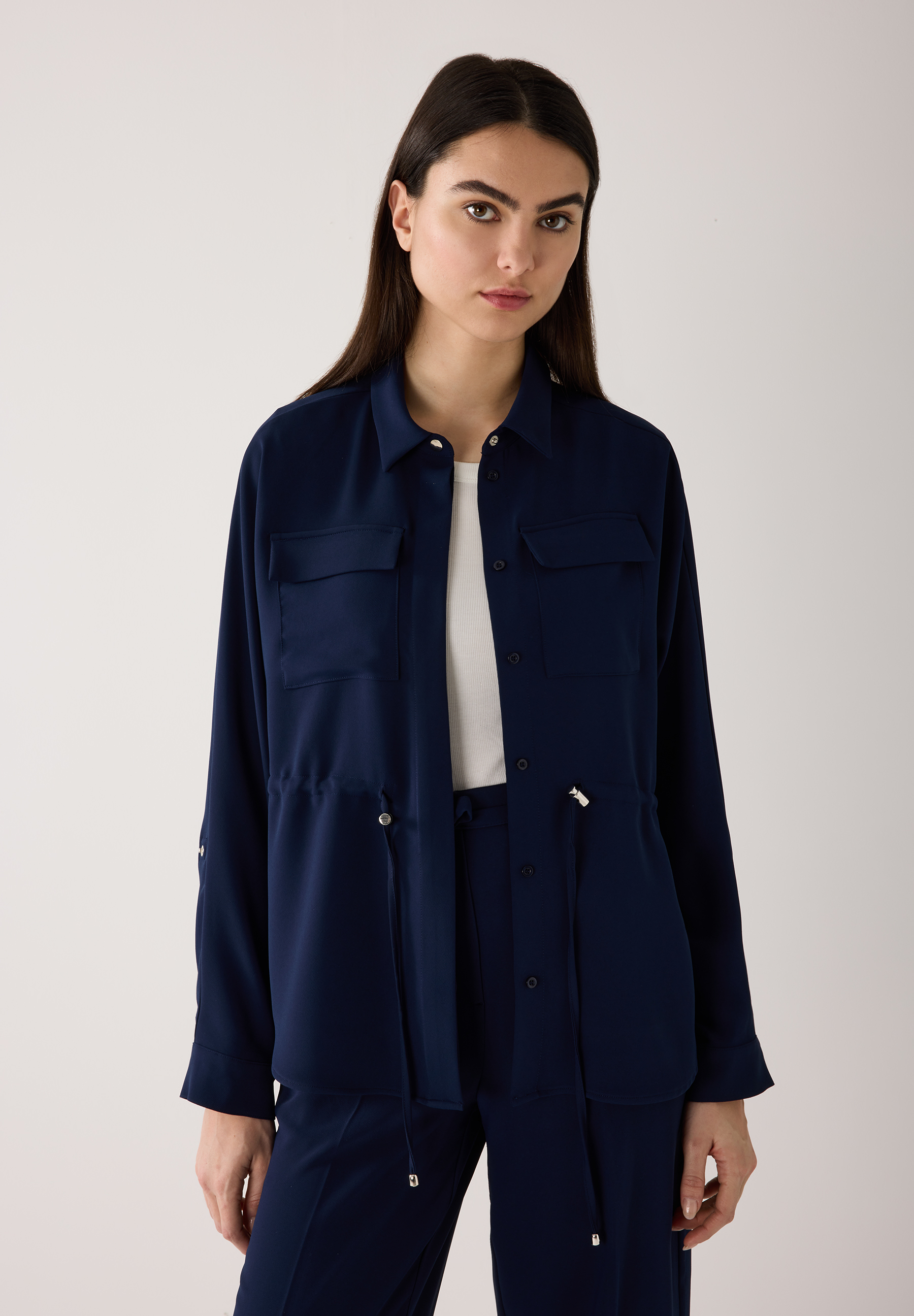Eine Frau mit einem marineblauen MORE & MORE Blazer aus fließender Webware, geschlossen mit Knöpfen.