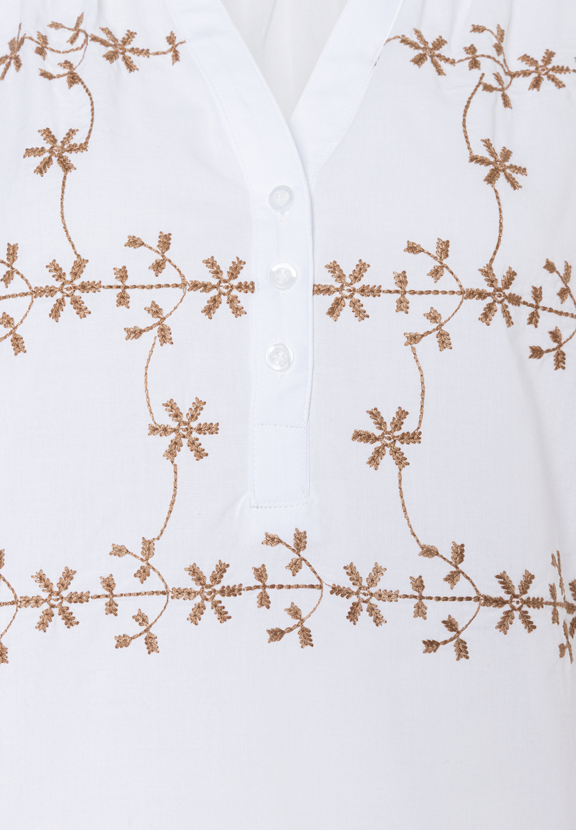 Nahaufnahme einer weißen MORE & MORE Bluse mit Knopfleiste und floralen Stickereien in Gold. Nahaufnahme einer weißen MORE & MORE Bluse mit Knopfleiste und floralen Stickereien in Gold.