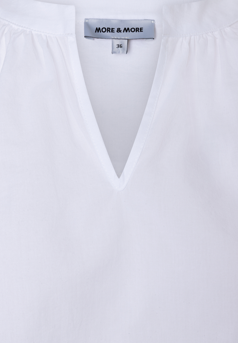 Detailaufnahme einer weißen MORE & MORE Bluse aus Baumwolle mit V-Ausschnitt und Größenetikett. Detailaufnahme einer weißen MORE & MORE Bluse aus Baumwolle mit V-Ausschnitt und Größenetikett.
