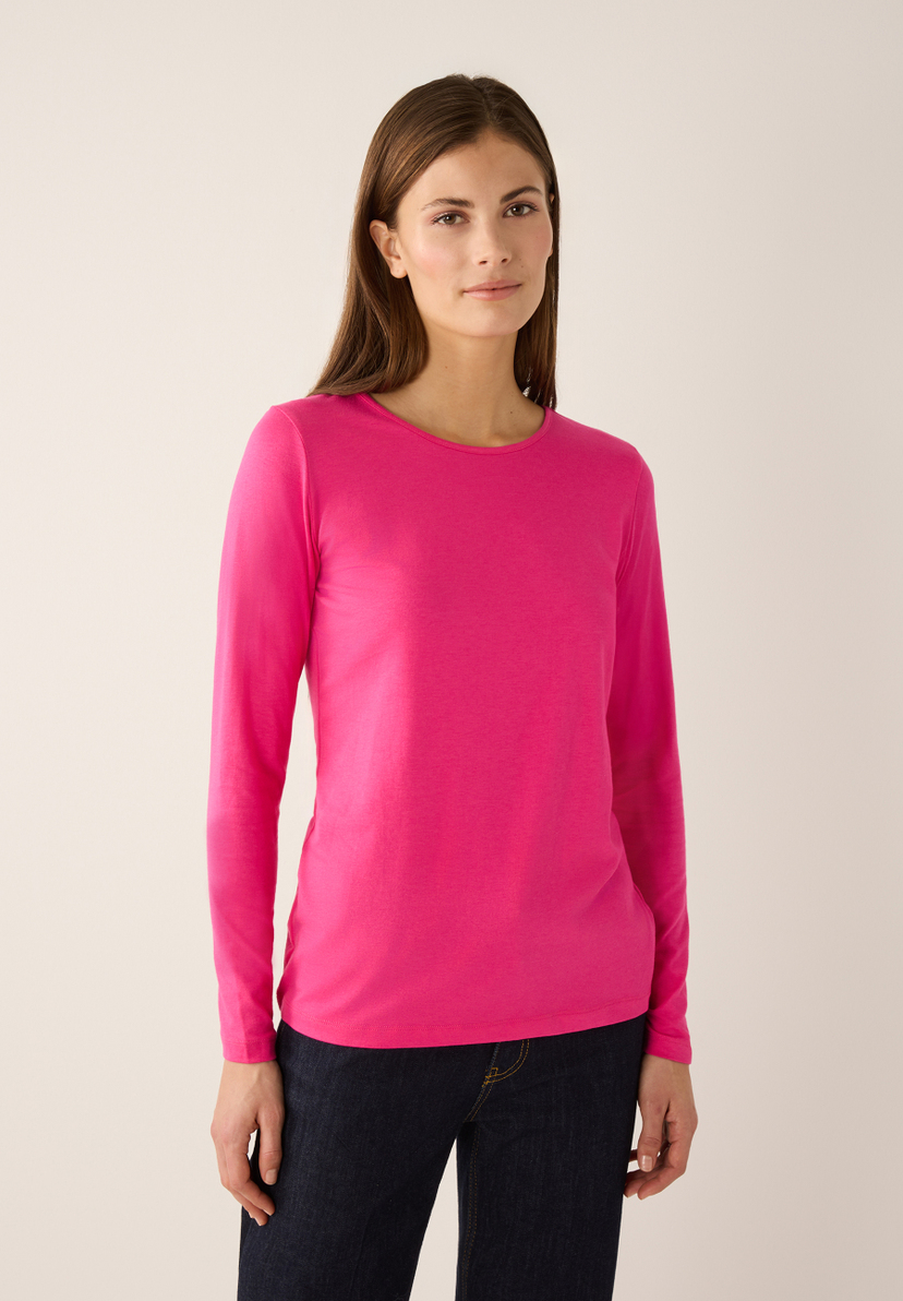 Eine Frau trägt ein pinkes, langärmliges MORE & MORE Shirt aus kühlendem Jersey und dunkle Jeans. Eine Frau trägt ein pinkes, langärmliges MORE & MORE Shirt aus kühlendem Jersey und dunkle Jeans.