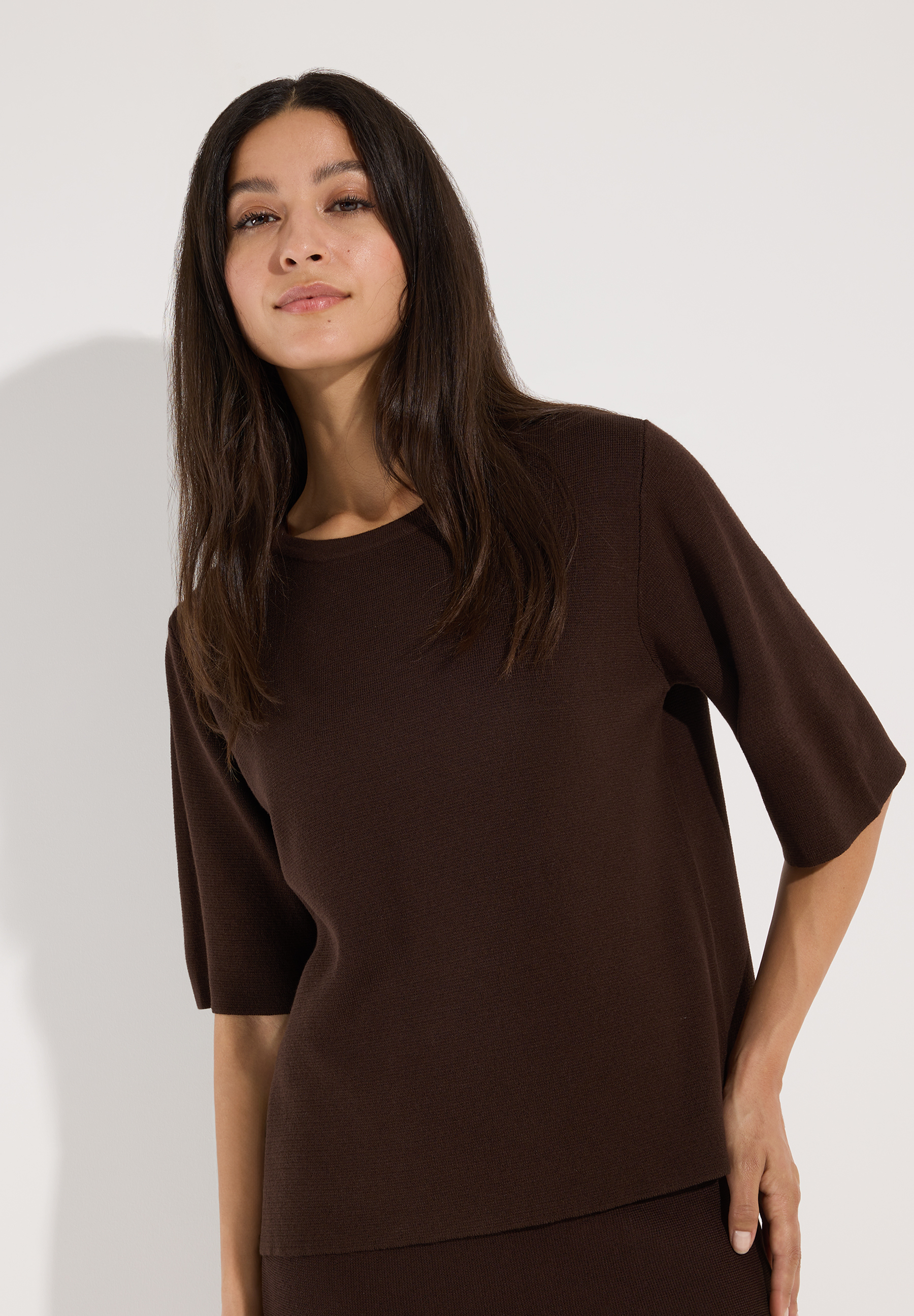 MORE & MORE Pullover: Eine Frau mit langen, dunklen Haaren trägt einen kurzärmeligen, gerippten, braunen Pullover.
