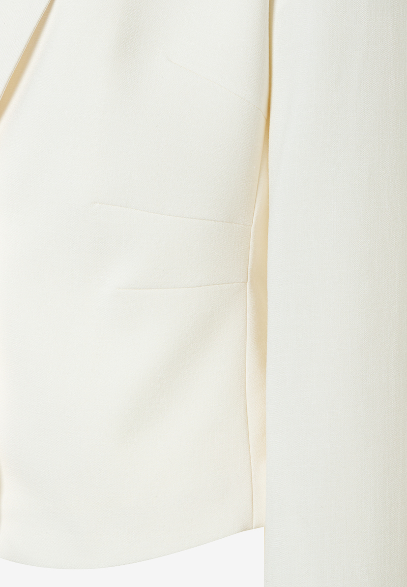 Detailaufnahme eines MORE & MORE Blazers in Creme mit angedeuteter Pattentasche und klaren Linien. Detailaufnahme eines MORE & MORE Blazers in Creme mit angedeuteter Pattentasche und klaren Linien.