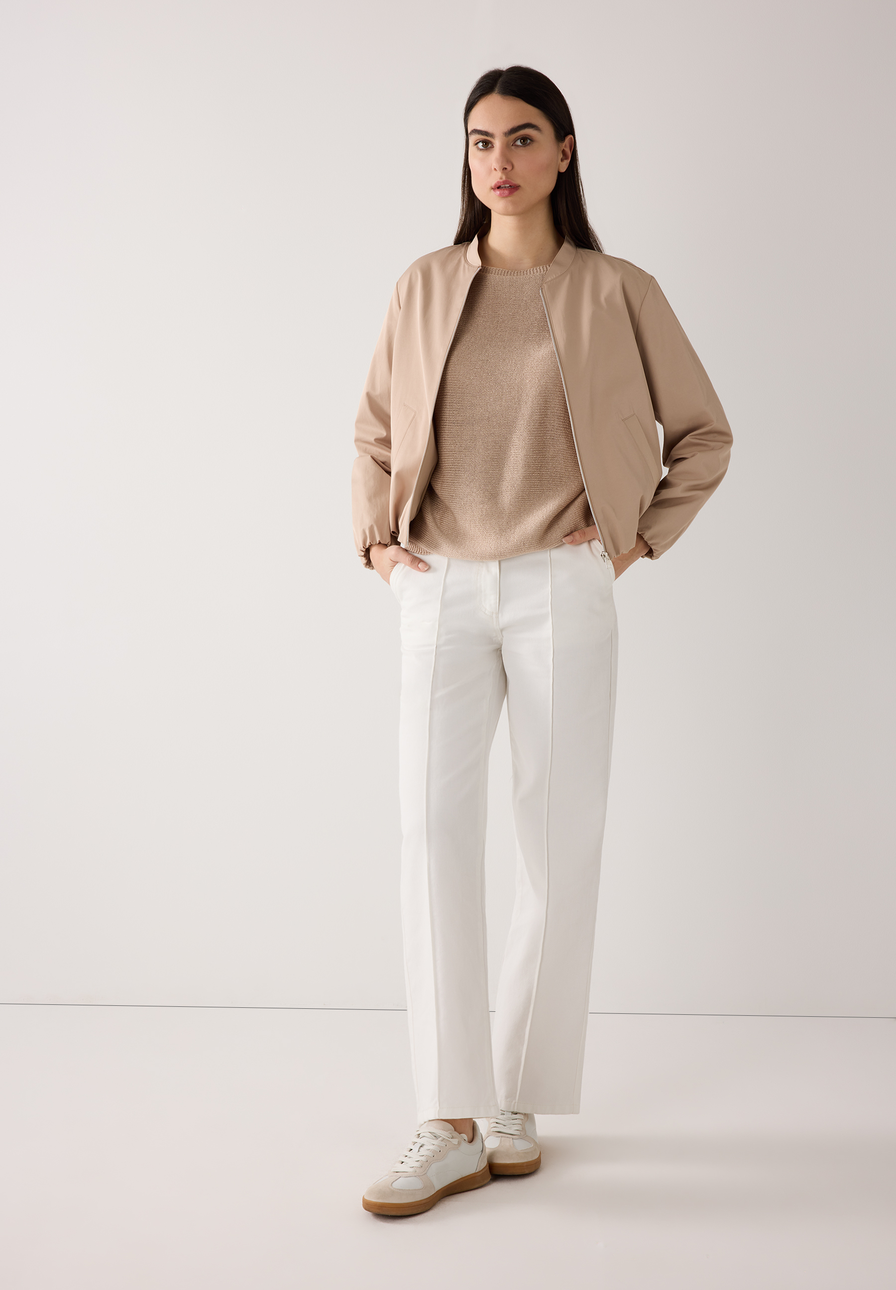 Eine Frau in MORE & MORE Oberteilen: Blazer und Rock, dazu Rollkragen und Stiefel vor neutralem Grund. Eine Frau in MORE & MORE Oberteilen: Blazer und Rock, dazu Rollkragen und Stiefel vor neutralem Grund.