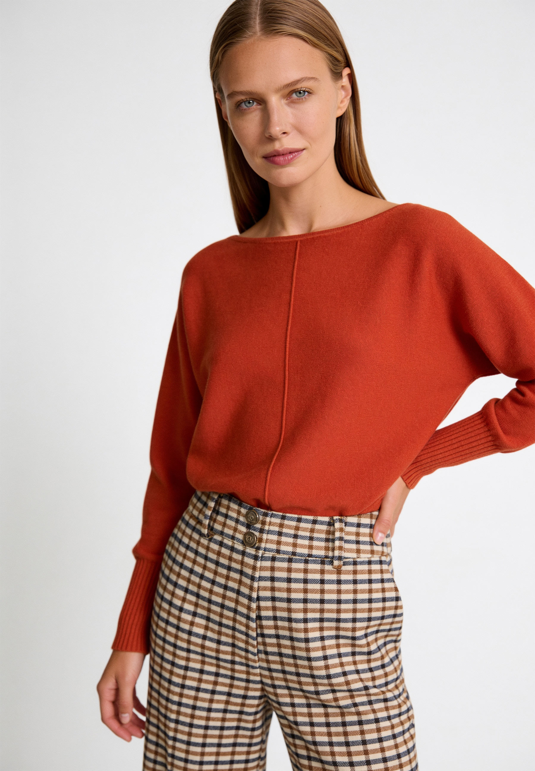 AI generated - MORE & MORE Feinstrick-Pullover in Rostrot. Model trägt eine Hose mit braun-weißem Karomuster.