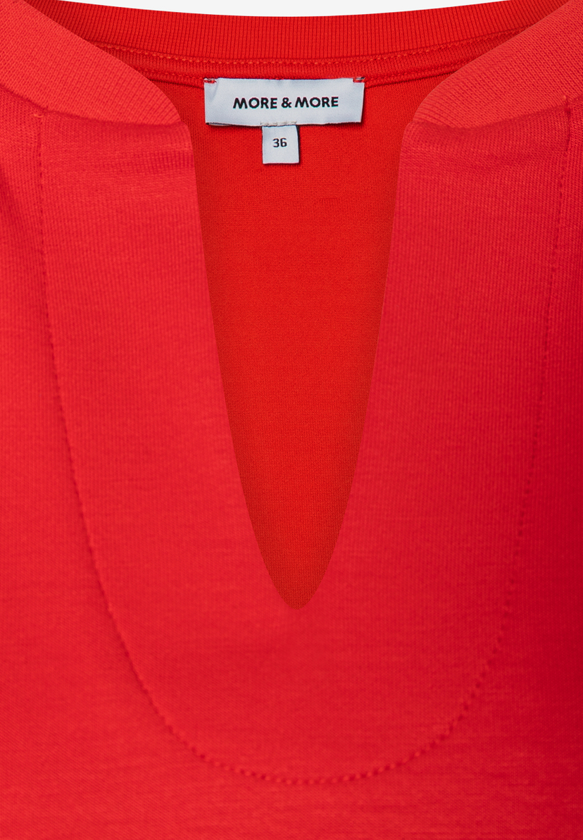 Nahaufnahme eines roten MORE & MORE Sweatshirts mit V-Ausschnitt und Größenetikett. Nahaufnahme eines roten MORE & MORE Sweatshirts mit V-Ausschnitt und Größenetikett.