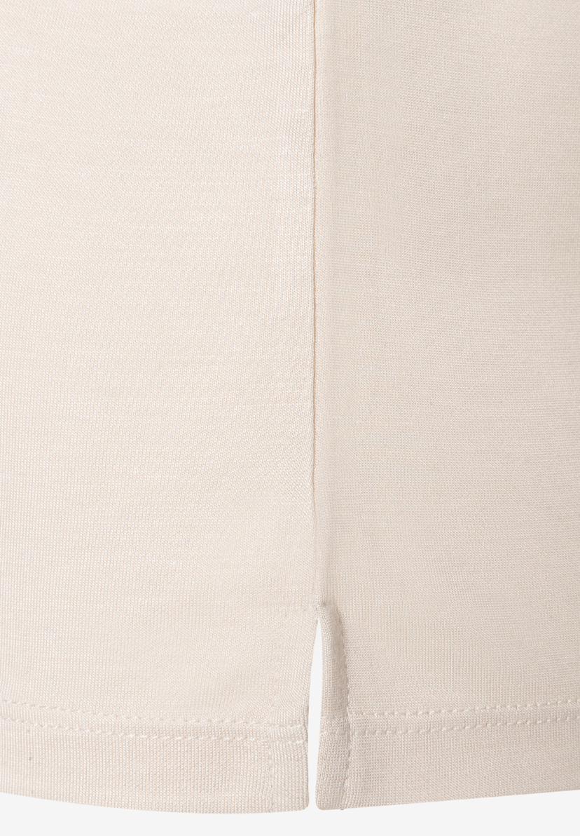 Nahaufnahme eines beigen MORE & MORE Oberteils aus Jersey mit kleinem Schlitz am Saum. Nahaufnahme eines beigen MORE & MORE Oberteils aus Jersey mit kleinem Schlitz am Saum.