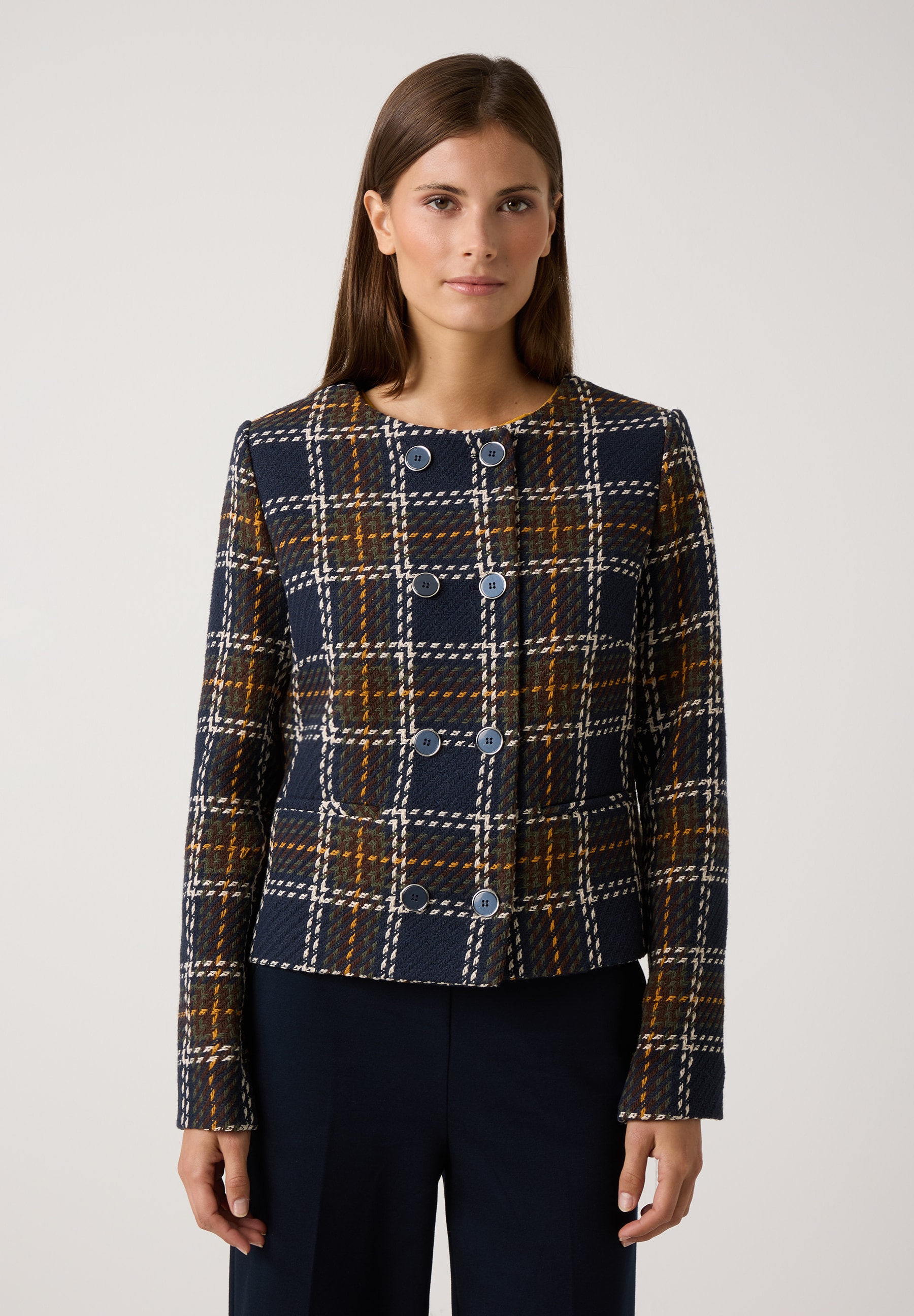 Eine Frau trägt einen MORE & MORE Blazer mit Karomuster in Blau, Braun und Gelb vor einem weißen Hintergrund. Eine Frau trägt einen MORE & MORE Blazer mit Karomuster in Blau, Braun und Gelb vor einem weißen Hintergrund.