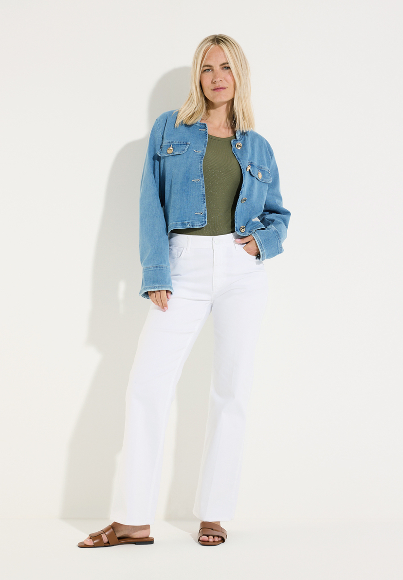 MORE & MORE Jeans: Blonde Frau in blauer Jeansjacke über grünem Top & weißer Hose. Trägt braune Sandalen, Hand in Hosentasche. MORE & MORE Jeans: Blonde Frau in blauer Jeansjacke über grünem Top & weißer Hose. Trägt braune Sandalen, Hand in Hosentasche.
