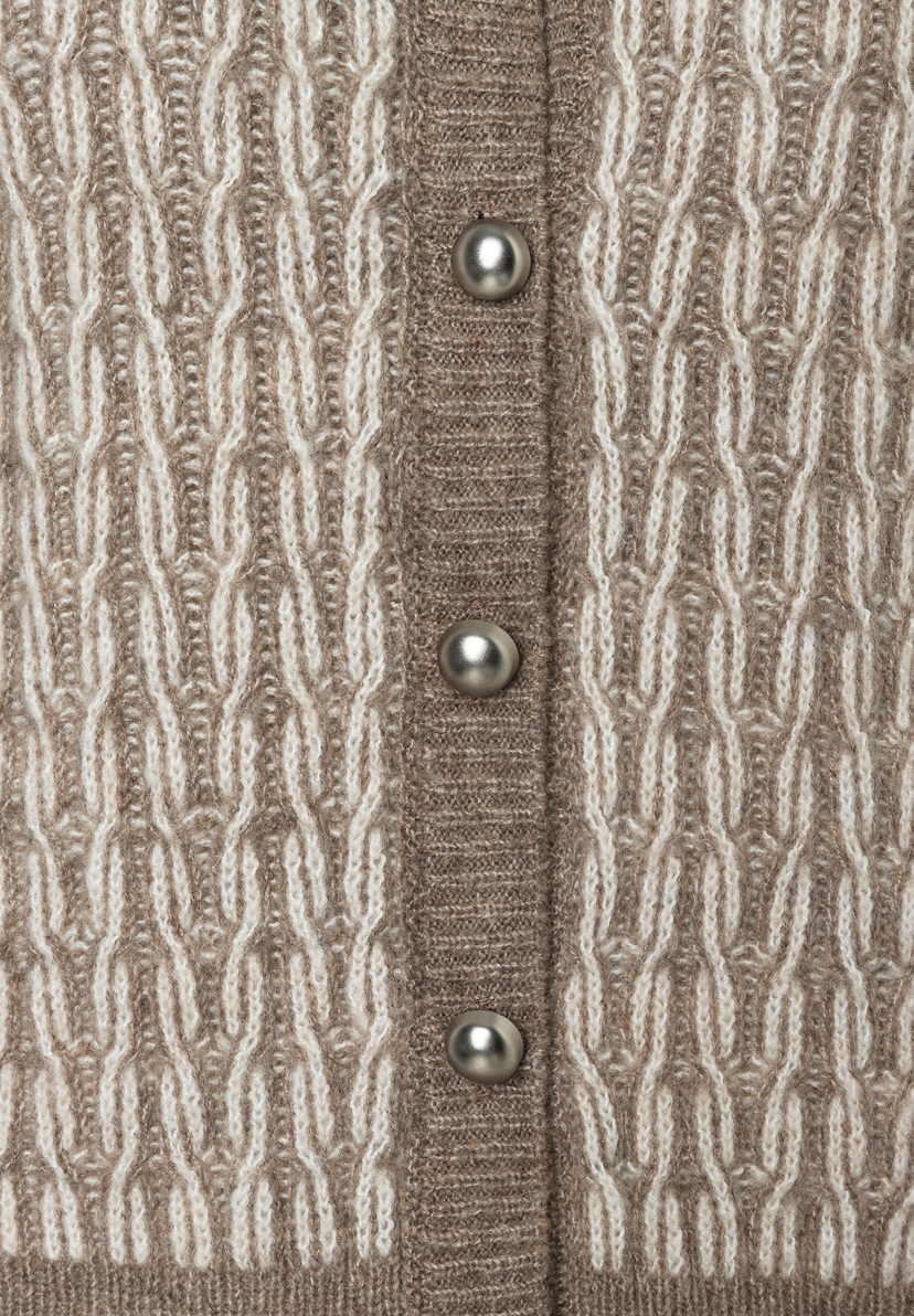 Nahaufnahme einer MORE & MORE Strickjacke mit Zopfmuster und silbernen Knöpfen. Das Material wirkt wärmend und hat einen weichen Griff. Nahaufnahme einer MORE & MORE Strickjacke mit Zopfmuster und silbernen Knöpfen. Das Material wirkt wärmend und hat einen weichen Griff.