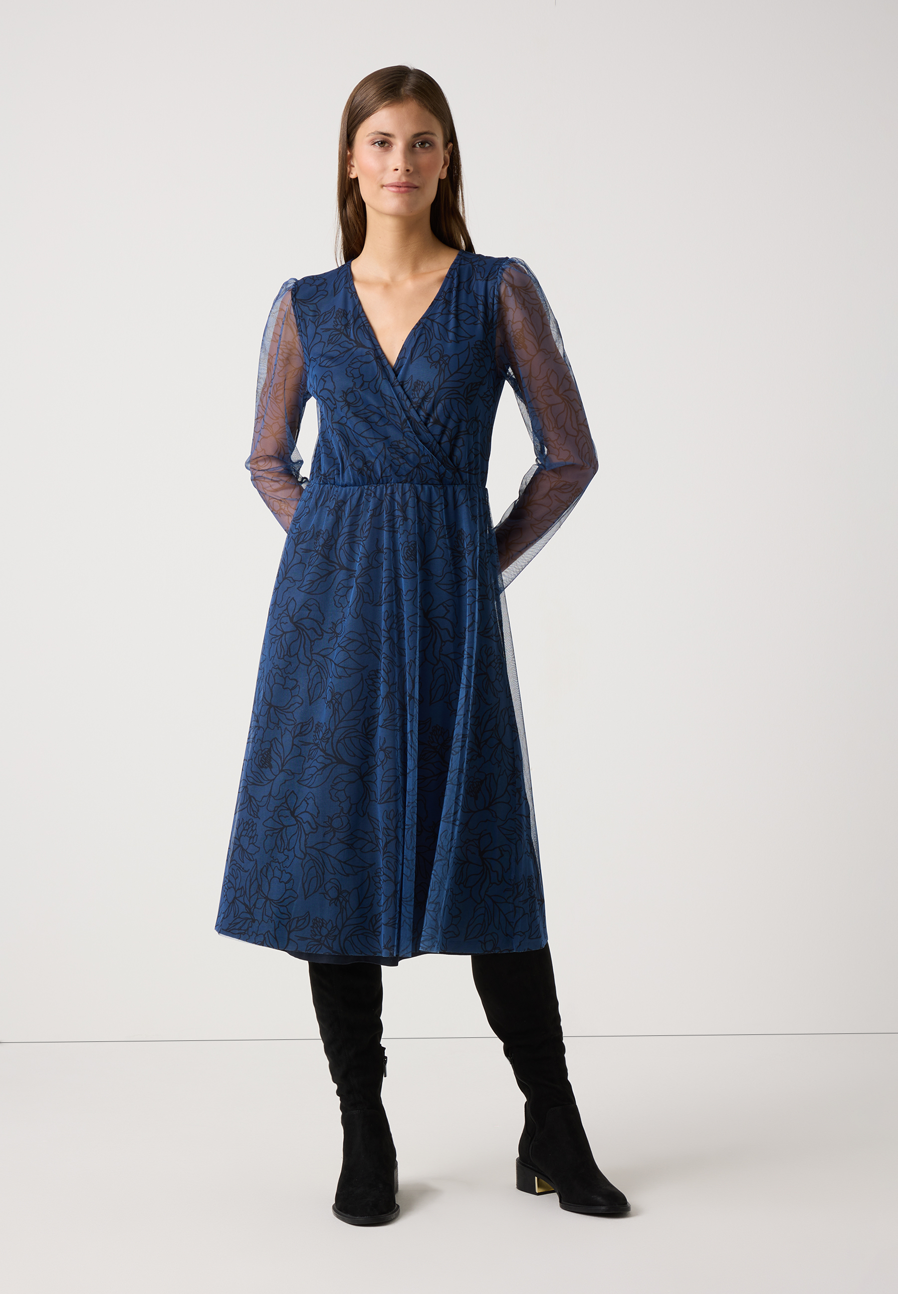 Eine Frau in einem blauen MORE & MORE Mesh-Kleid mit Blumenmuster und langen Ärmeln.