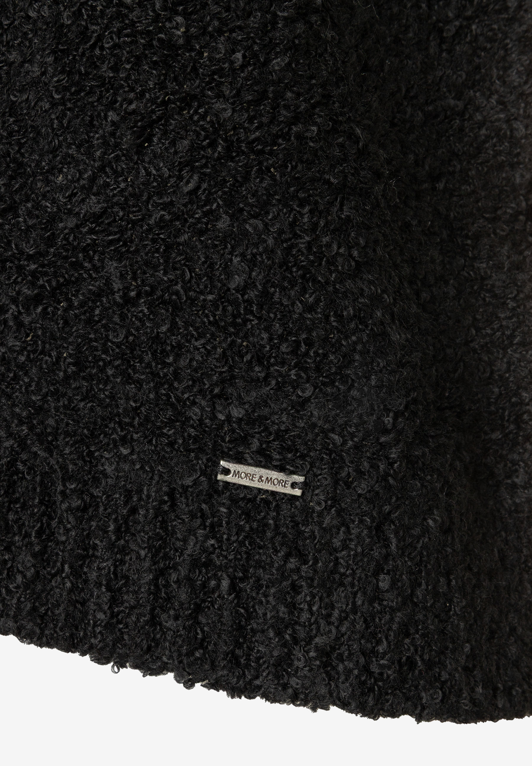 MORE & MORE schwarzer Bouclé-Pullover mit Metall-Logo-Emblem, Nahaufnahme des gekräuselten, voluminösen Stoffes.