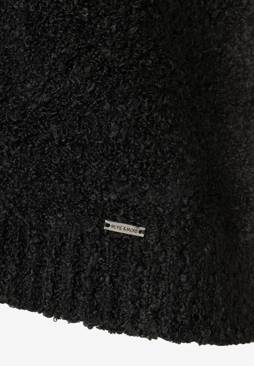 MORE & MORE schwarzer Bouclé-Pullover mit Metall-Logo-Emblem, Nahaufnahme des gekräuselten, voluminösen Stoffes.