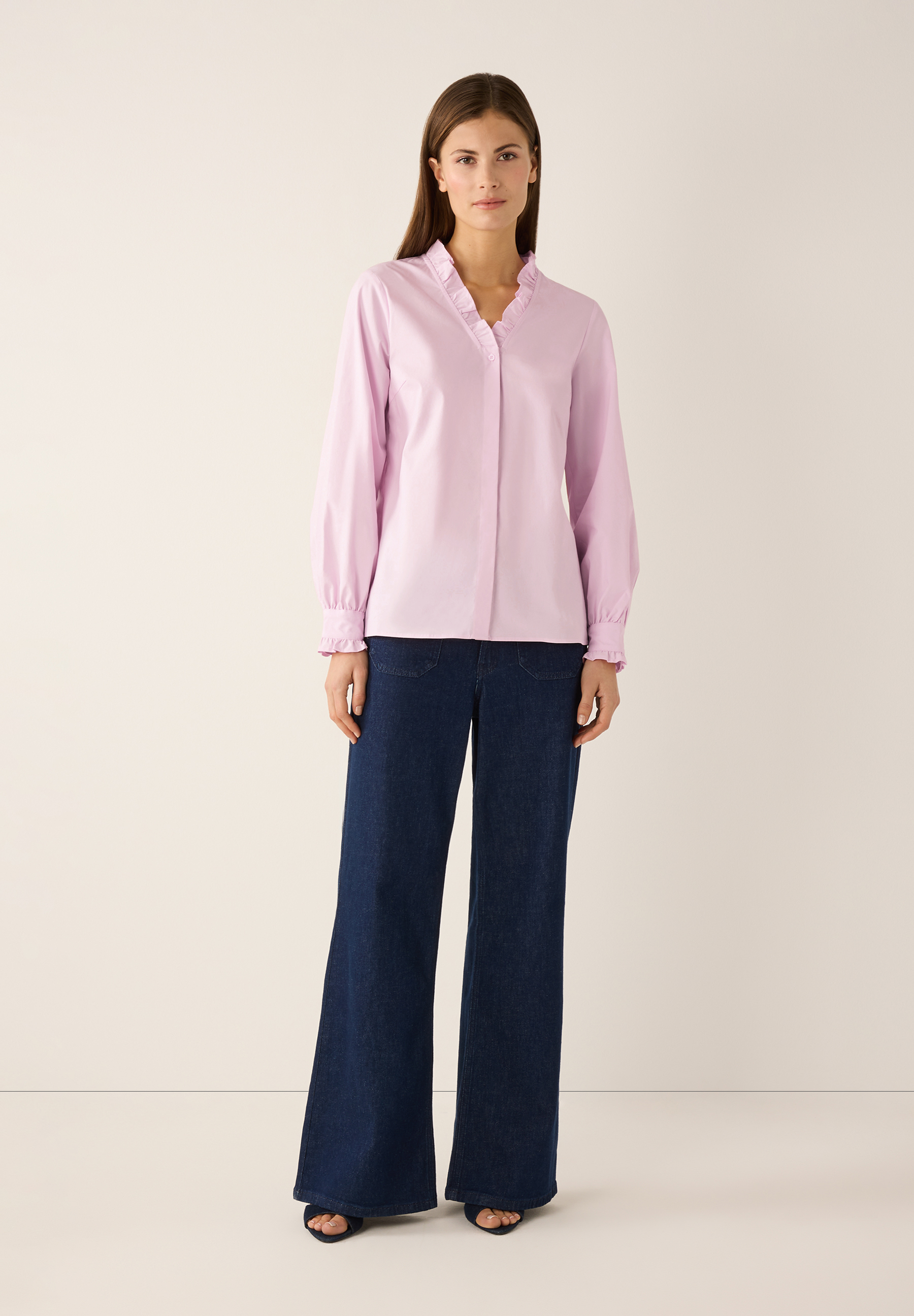 Eine Frau zeigt eine rosa MORE & MORE Bluse mit Rüschen und weite Jeans. Eine Frau zeigt eine rosa MORE & MORE Bluse mit Rüschen und weite Jeans.