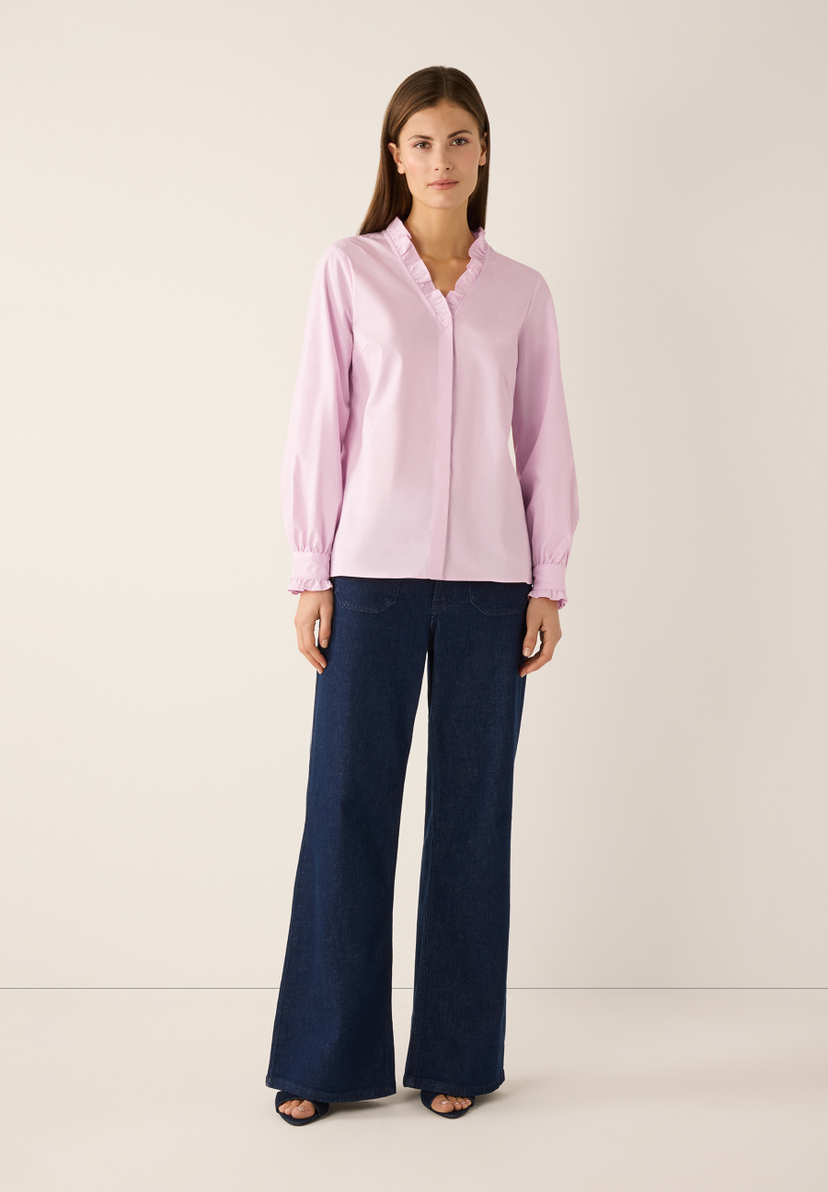 Eine Frau zeigt eine rosa MORE & MORE Bluse mit Rüschen und weite Jeans. Eine Frau zeigt eine rosa MORE & MORE Bluse mit Rüschen und weite Jeans.