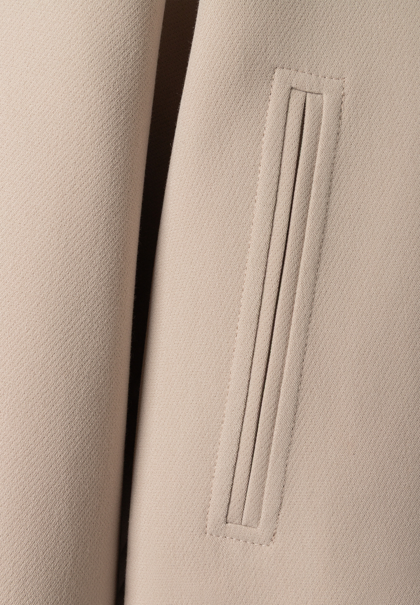 Detailansicht des MORE & MORE Blazers: Eine eckige Pattentasche mit vertikalen Ziernähten ist auf dem beigen Stoff zu sehen. Detailansicht des MORE & MORE Blazers: Eine eckige Pattentasche mit vertikalen Ziernähten ist auf dem beigen Stoff zu sehen.