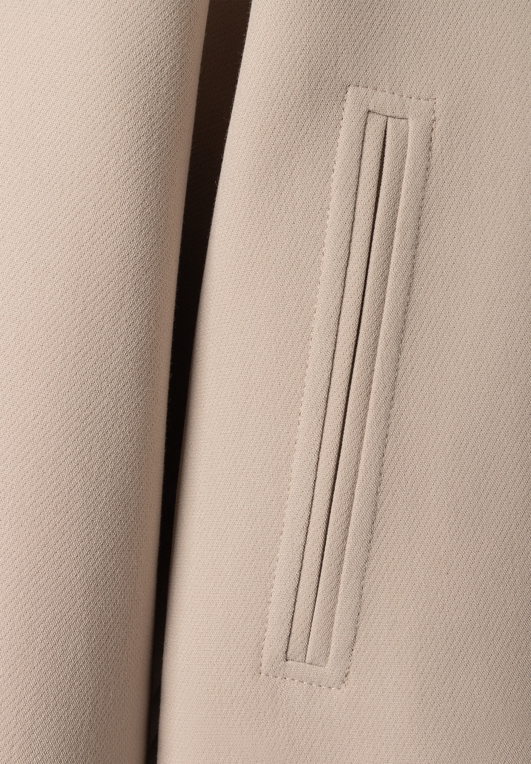 Detailansicht des MORE & MORE Blazers: Eine eckige Pattentasche mit vertikalen Ziernähten ist auf dem beigen Stoff zu sehen. Detailansicht des MORE & MORE Blazers: Eine eckige Pattentasche mit vertikalen Ziernähten ist auf dem beigen Stoff zu sehen.