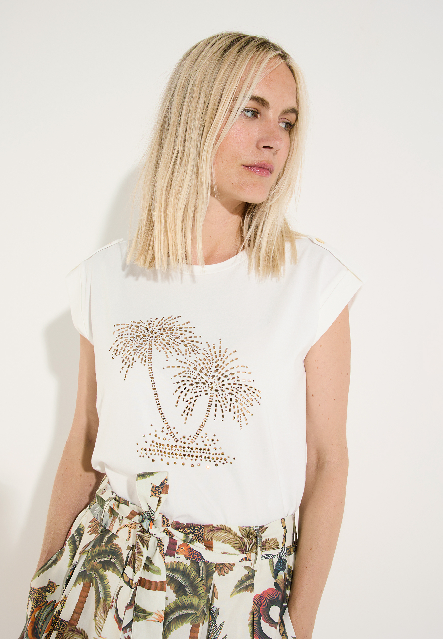 MORE & MORE T-Shirt in Weiß mit Strasspalmen und beigem Musterrock. Eine Frau mit blonden Haaren trägt das Outfit.