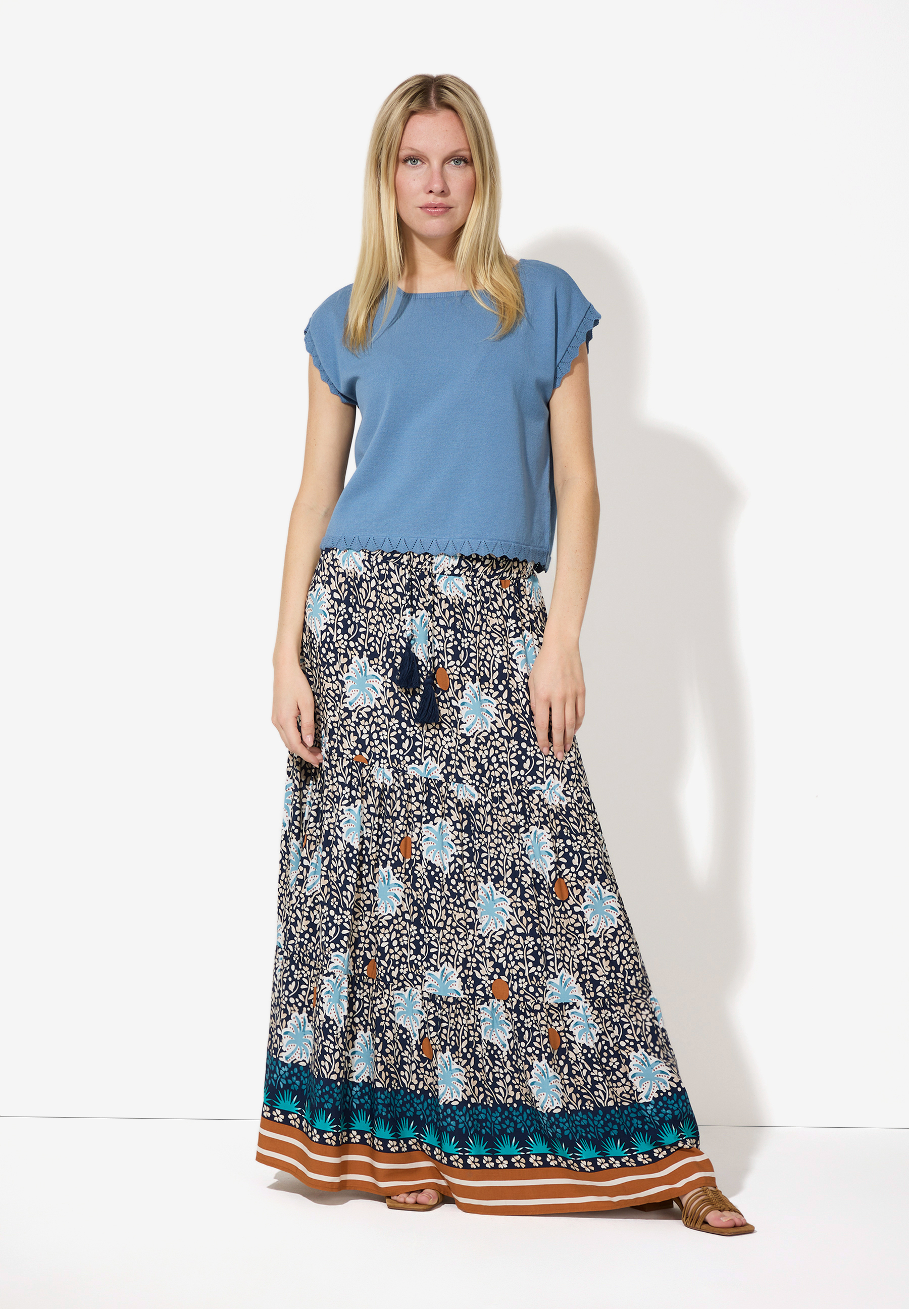 Eine Frau in einem blauen Top und einem langen, geblümten MORE & MORE Rock aus Webware mit angenehmem Tragekomfort. Eine Frau in einem blauen Top und einem langen, geblümten MORE & MORE Rock aus Webware mit angenehmem Tragekomfort.