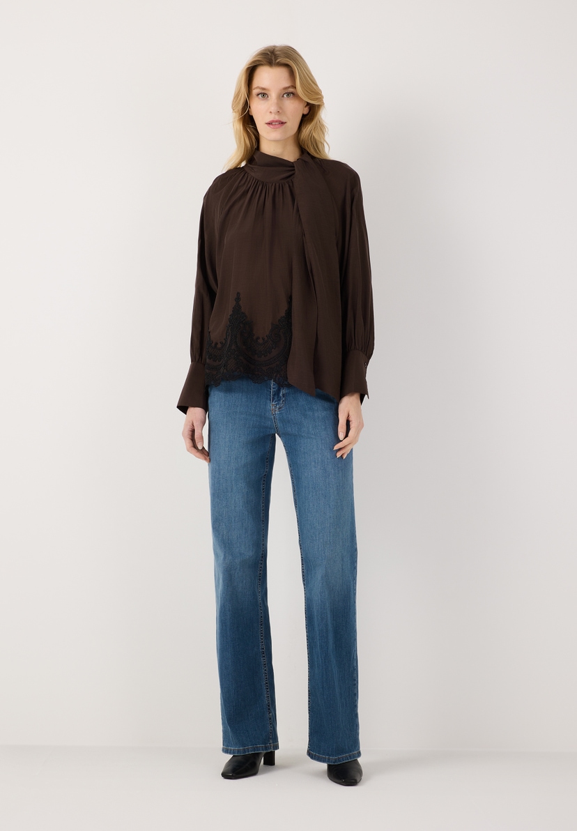MORE & MORE Bluse: Eine blonde Frau trägt eine braune Bluse mit Krawattendetail und Spitzensaum zu Jeans. MORE & MORE Bluse: Eine blonde Frau trägt eine braune Bluse mit Krawattendetail und Spitzensaum zu Jeans.