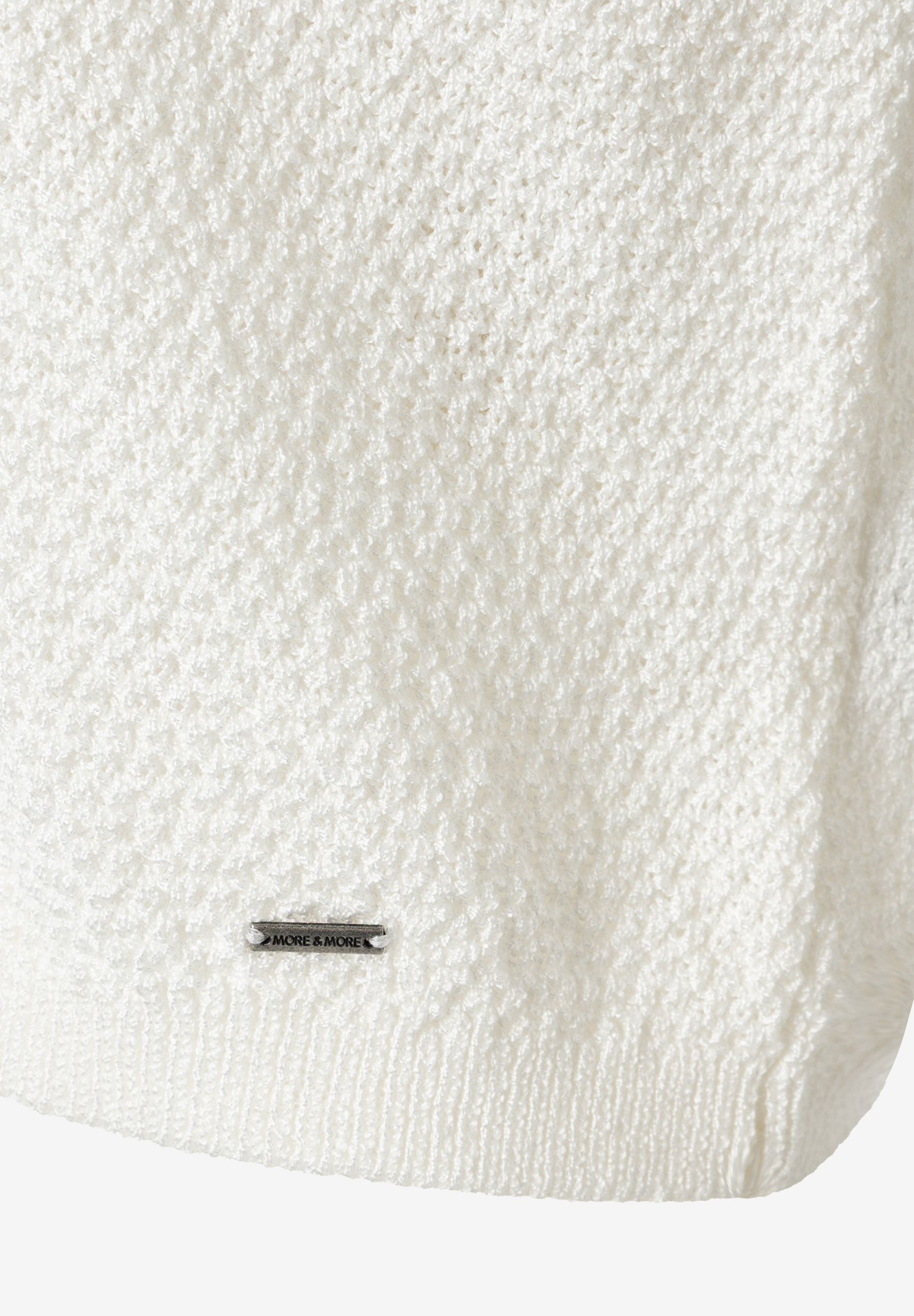 Nahaufnahme eines weißen Strickpullovers von MORE & MORE mit kleinem Marken-Logo. Nahaufnahme eines weißen Strickpullovers von MORE & MORE mit kleinem Marken-Logo.