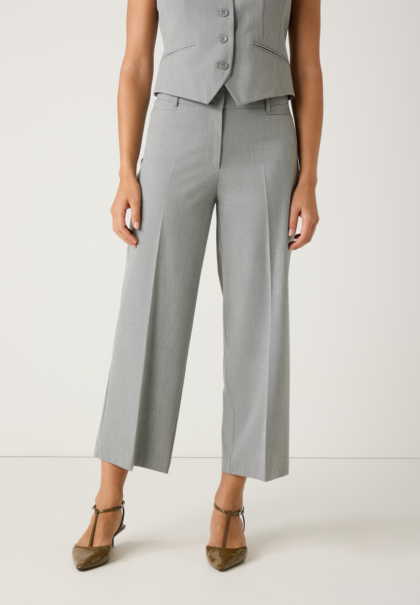 Eine Person mit MORE & MORE Hose. Die graue Hose ist knöchellang und locker geschnitten. Dazu trägt die Person braune Mary Jane Schuhe. Eine Person mit MORE & MORE Hose. Die graue Hose ist knöchellang und locker geschnitten. Dazu trägt die Person braune Mary Jane Schuhe.