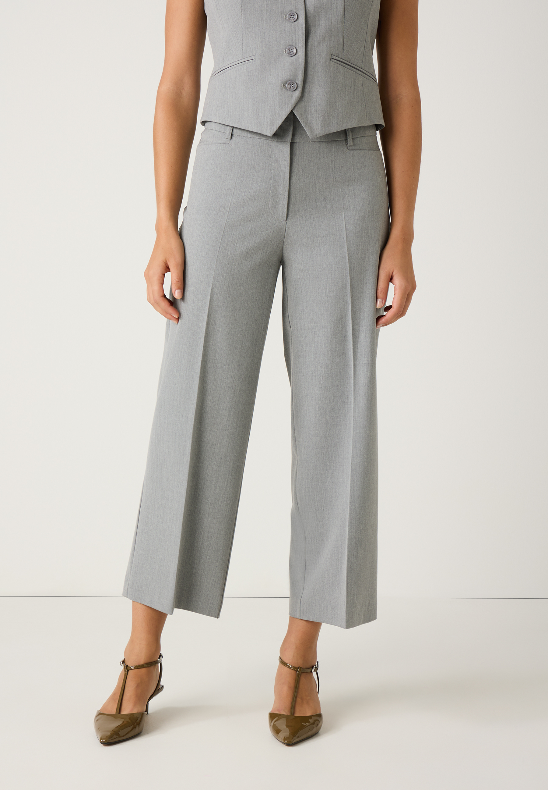 Eine Person mit MORE & MORE Hose. Die graue Hose ist knöchellang und locker geschnitten. Dazu trägt die Person braune Mary Jane Schuhe.