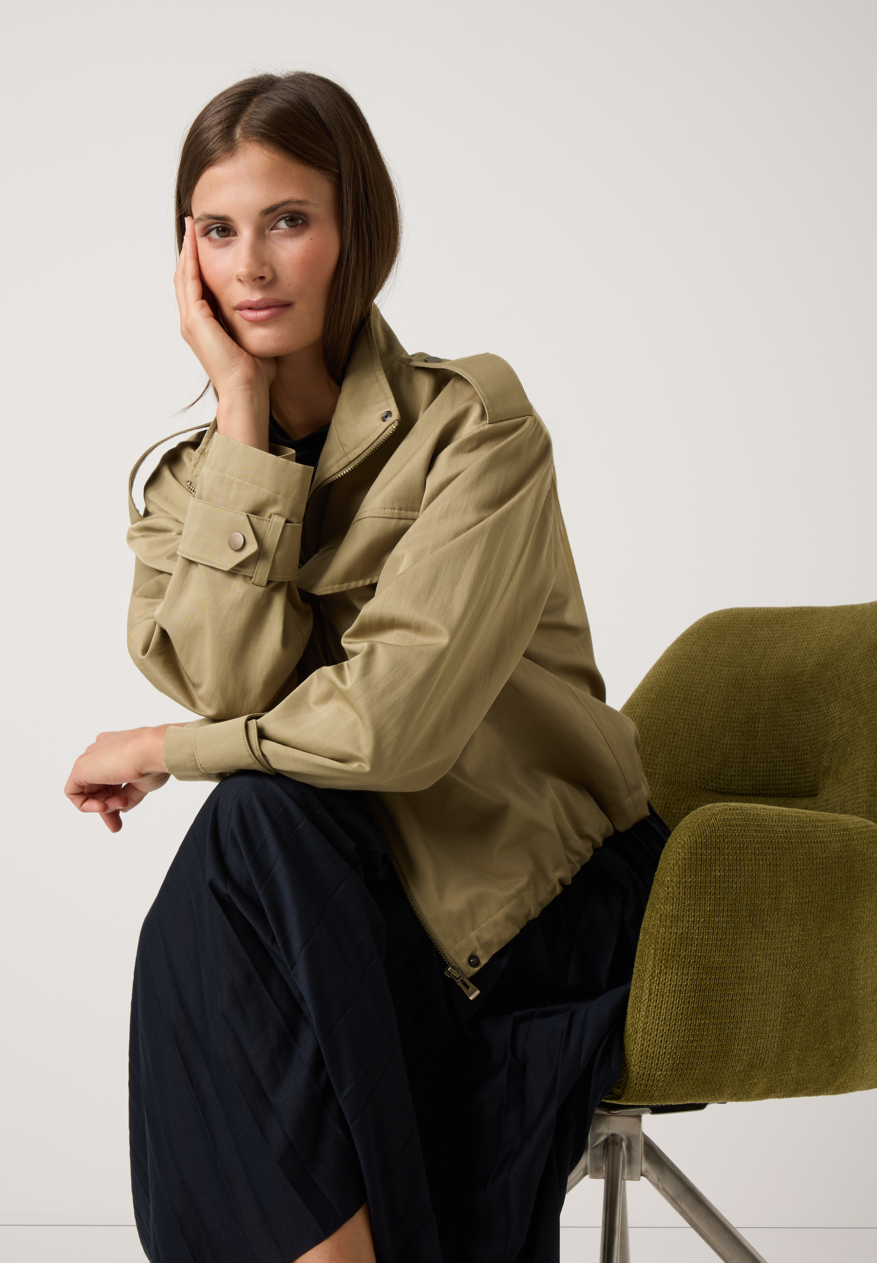 Eine Frau sitzt in einem olivgrünen Sessel und trägt ein MORE & MORE Oberteil mit Jersey-Material. Eine Frau sitzt in einem olivgrünen Sessel und trägt ein MORE & MORE Oberteil mit Jersey-Material.