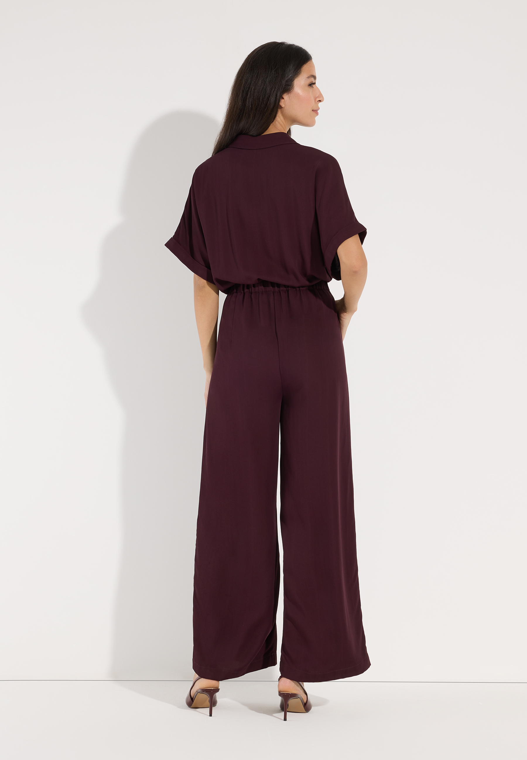 MORE & MORE Jumpsuit aus fließendem Material in Weinrot. Das Model trägt den Jumpsuit von hinten. MORE & MORE Jumpsuit aus fließendem Material in Weinrot. Das Model trägt den Jumpsuit von hinten.