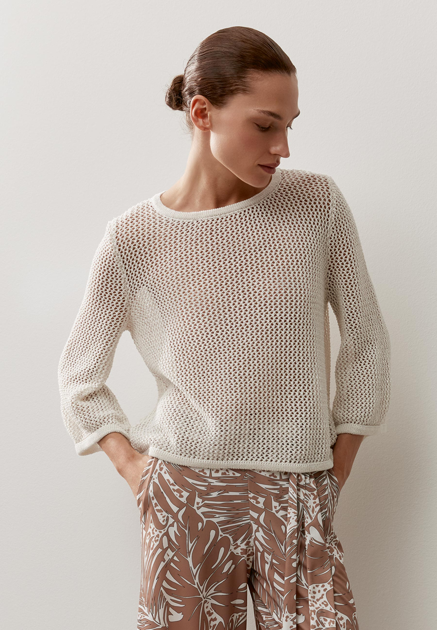 Eine Frau mit MORE & MORE Lochstrick-Pullover mit 3/4-Ärmeln posiert vor einer weißen Wand.
