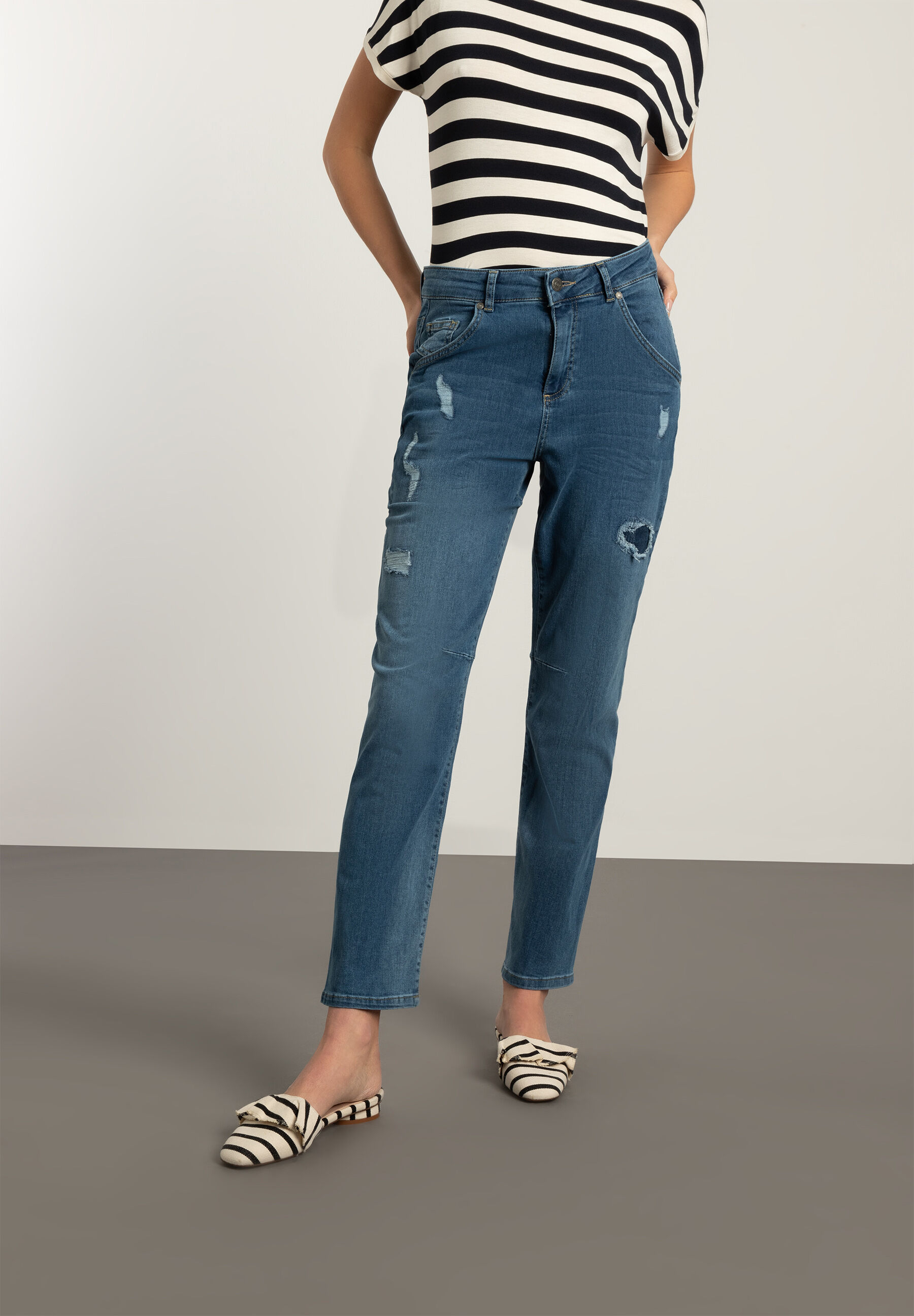Eine Frau mit MORE & MORE Jeans aus Denim-Stretchstoff mit Rissen, kombiniert mit einem gestreiften Oberteil.