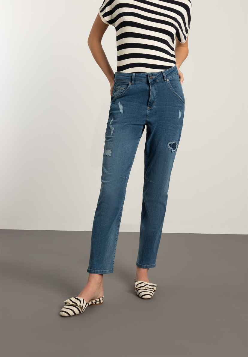 Eine Frau mit MORE & MORE Jeans aus Denim-Stretchstoff mit Rissen, kombiniert mit einem gestreiften Oberteil. Eine Frau mit MORE & MORE Jeans aus Denim-Stretchstoff mit Rissen, kombiniert mit einem gestreiften Oberteil.