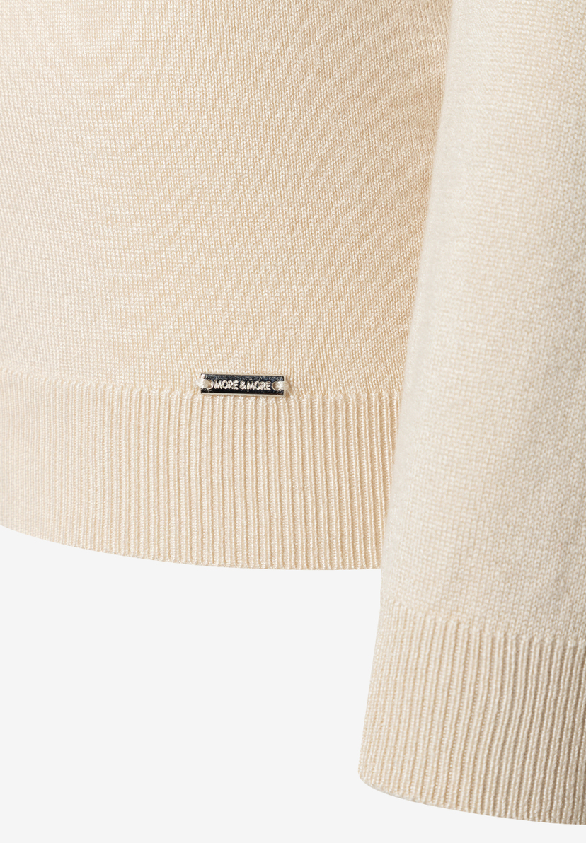 MORE & MORE Feinstrickpullover in Creme mit Rippbündchen, Nahaufnahme des Logos am Saum.