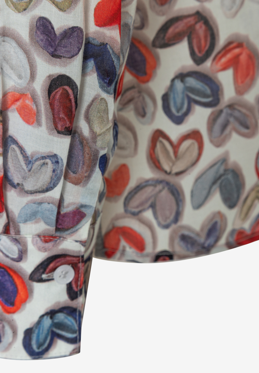 Detailansicht einer MORE & MORE Bluse mit buntem Herzmuster und Knopf am Ärmel. Detailansicht einer MORE & MORE Bluse mit buntem Herzmuster und Knopf am Ärmel.