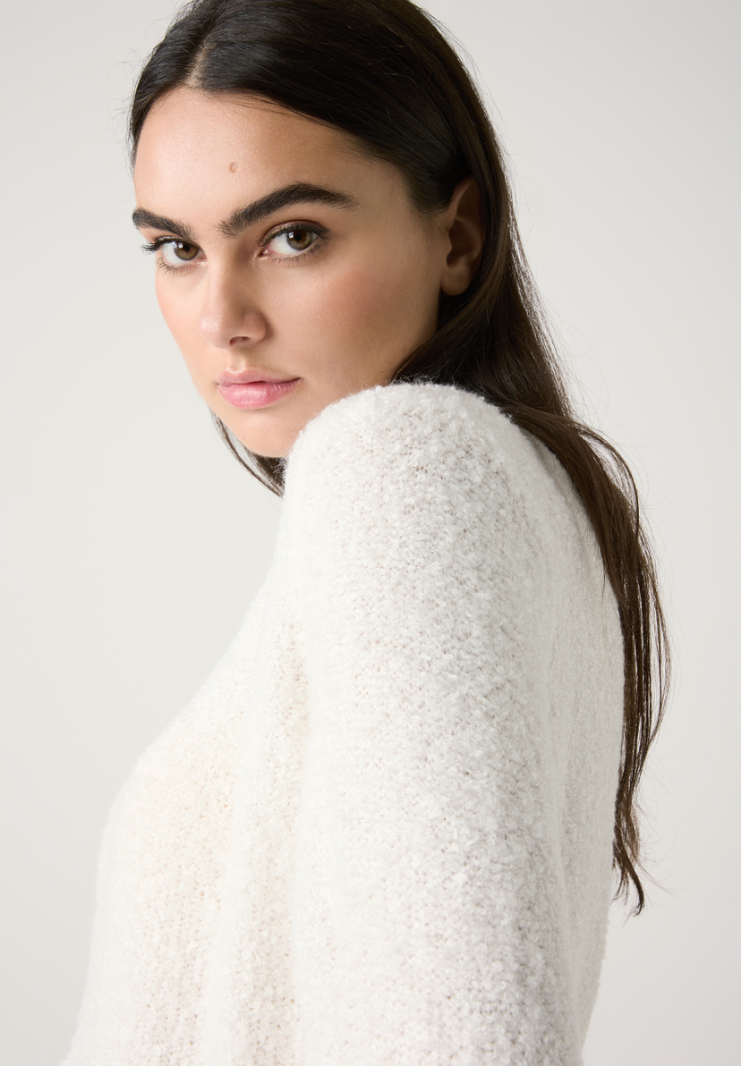 Eine Frau mit langen dunklen Haaren trägt einen weißen MORE & MORE Bouclé-Pullover und blickt über ihre Schulter. Eine Frau mit langen dunklen Haaren trägt einen weißen MORE & MORE Bouclé-Pullover und blickt über ihre Schulter.