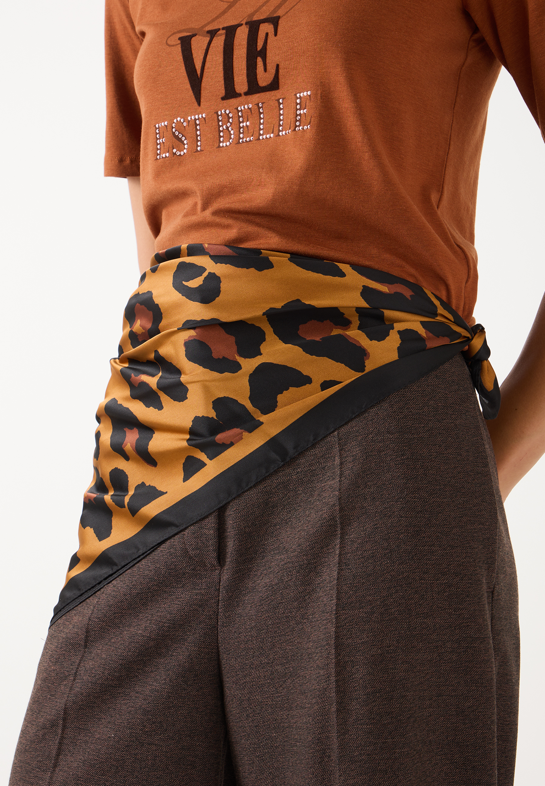 MORE & MORE Accessoire: Ein brauner Gürtel mit Leopardenmuster ist um eine braune Hose gebunden, das Oberteil hat eine Aufschrift.