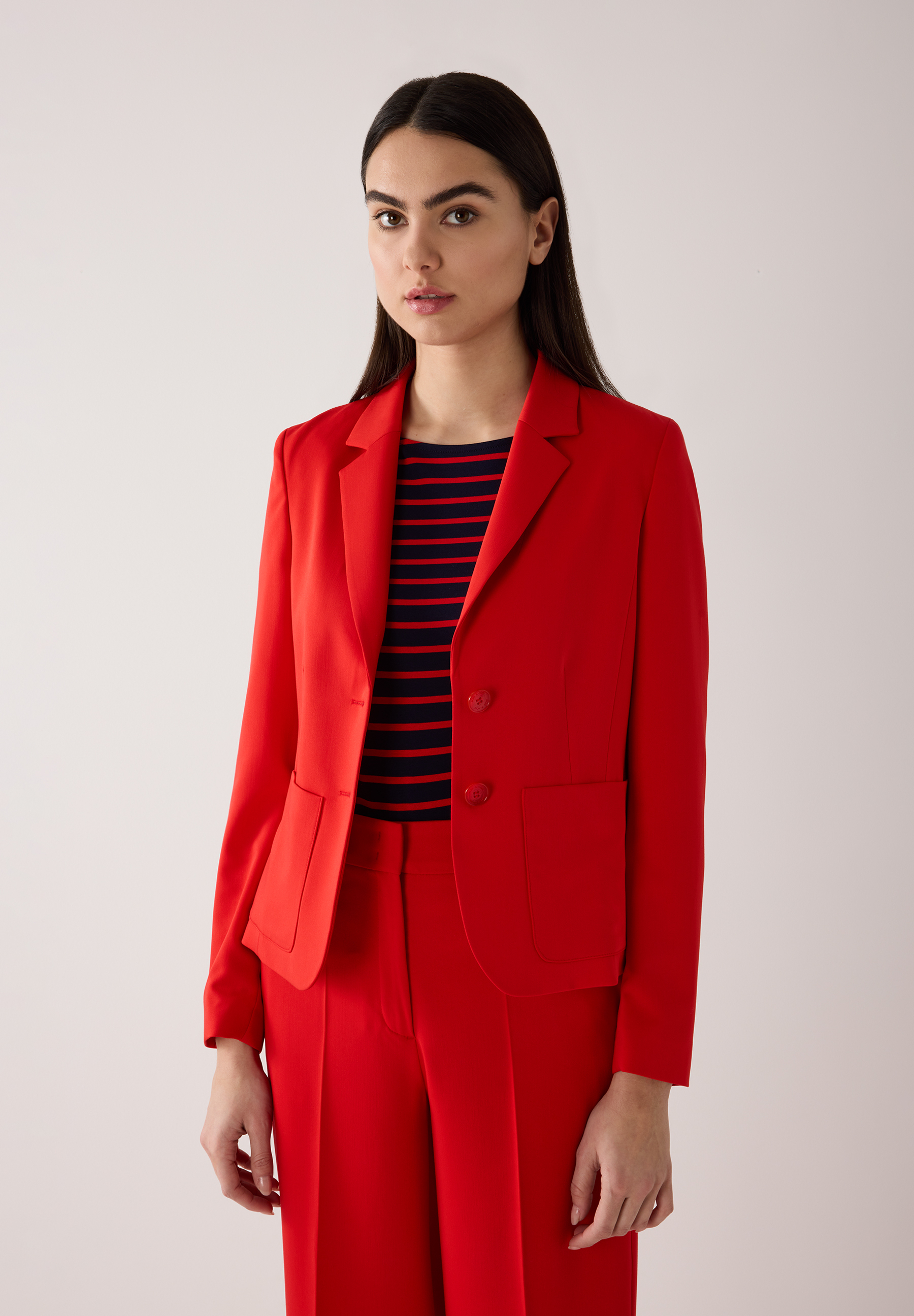 Eine Frau trägt einen roten MORE & MORE Blazer mit Webware und ein gestreiftes Oberteil.