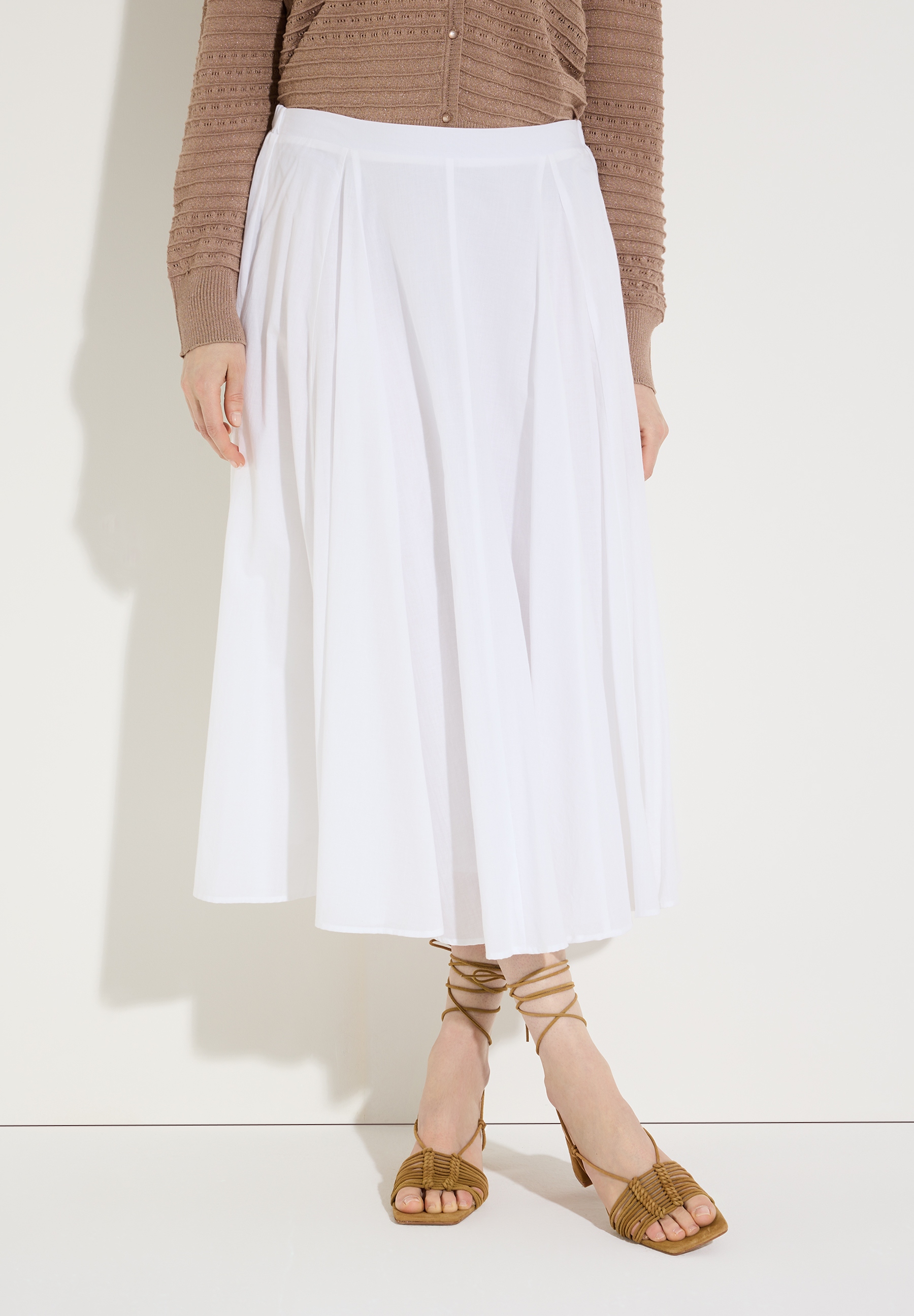 Ein weißer Rock von MORE & MORE fällt weich, kombiniert mit einer Jeansjacke mit Spitze und Sandalen.