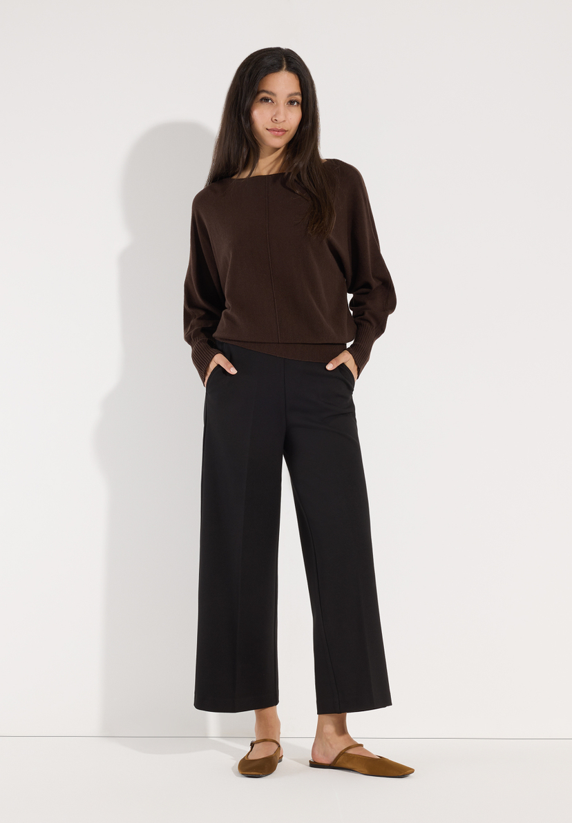 MORE & MORE Pullover: Eine Frau trägt einen braunen Strickpullover und schwarze Cropped-Hosen, die eine elegante Silhouette bilden. MORE & MORE Pullover: Eine Frau trägt einen braunen Strickpullover und schwarze Cropped-Hosen, die eine elegante Silhouette bilden.