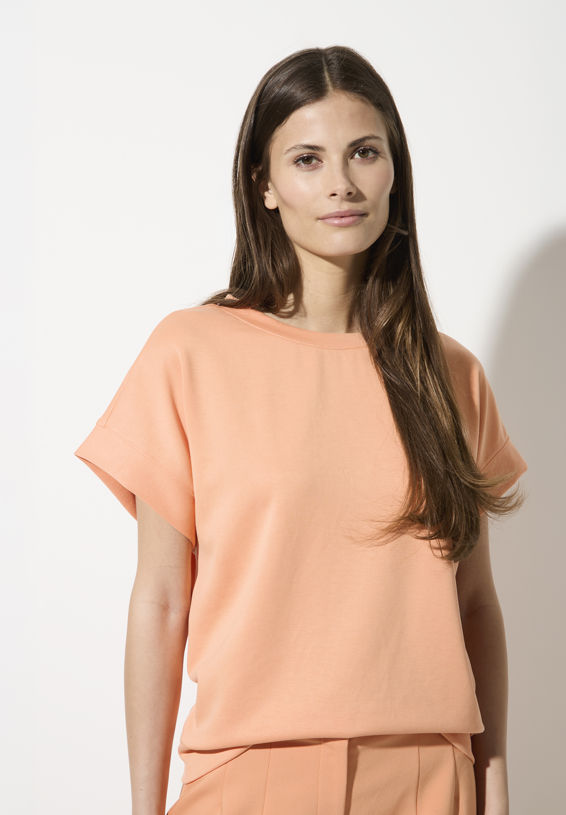 Eine Frau trägt ein lachsfarbenes MORE & MORE Sweatshirt-Oberteil.