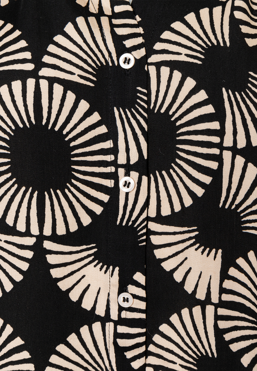 Detailaufnahme einer MORE & MORE Bluse mit schwarzem Muster und hellen, fließenden Akzenten. Weiße Knöpfe. Detailaufnahme einer MORE & MORE Bluse mit schwarzem Muster und hellen, fließenden Akzenten. Weiße Knöpfe.