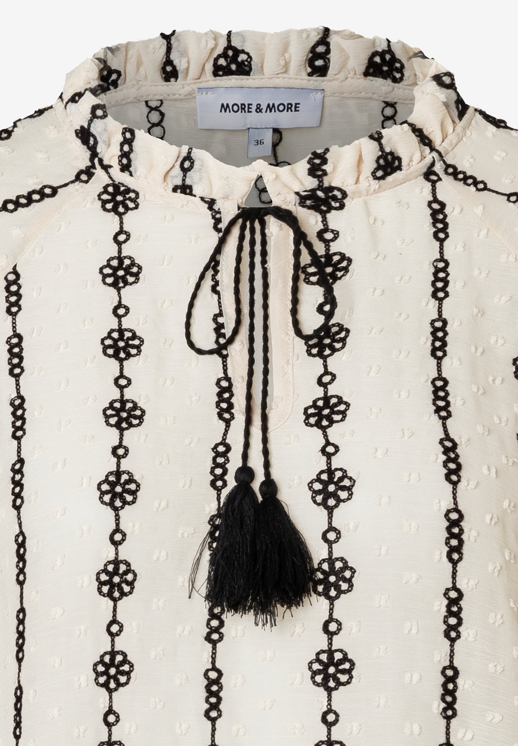 Detailaufnahme einer MORE & MORE Bluse mit Quasten und Lochmuster. Detailaufnahme einer MORE & MORE Bluse mit Quasten und Lochmuster.