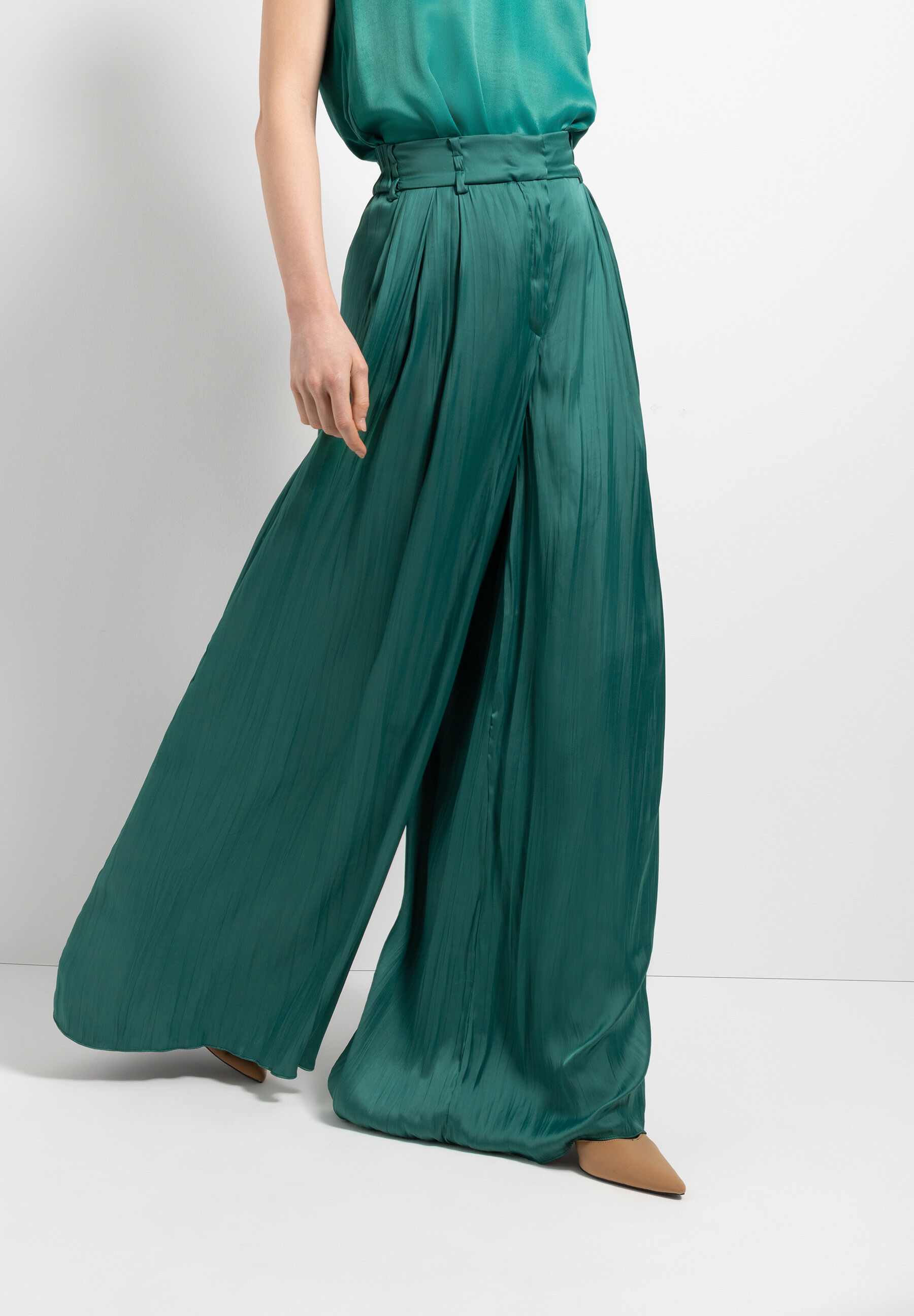 Eine Frau trägt eine grüne Hose von MORE & MORE mit weitem Bein und Bundfalten. Dazu braune Schuhe.
