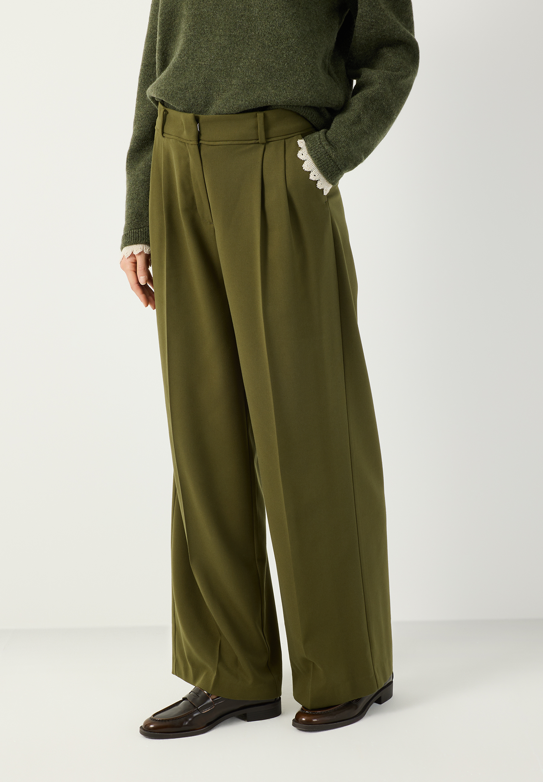 MORE & MORE olivgrüne Hose mit weitem Bein und Bundfalten, kombiniert mit einem dunkelgrünen Strickpullover und Loafers. MORE & MORE olivgrüne Hose mit weitem Bein und Bundfalten, kombiniert mit einem dunkelgrünen Strickpullover und Loafers.