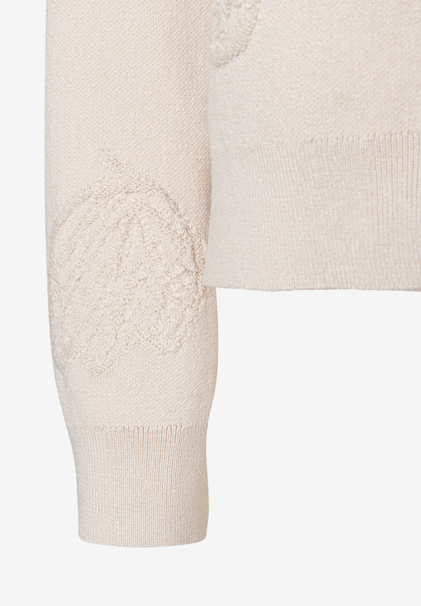 Detailaufnahme eines hellen MORE & MORE Strickpullovers mit Zopfmuster am Ärmel. Detailaufnahme eines hellen MORE & MORE Strickpullovers mit Zopfmuster am Ärmel.