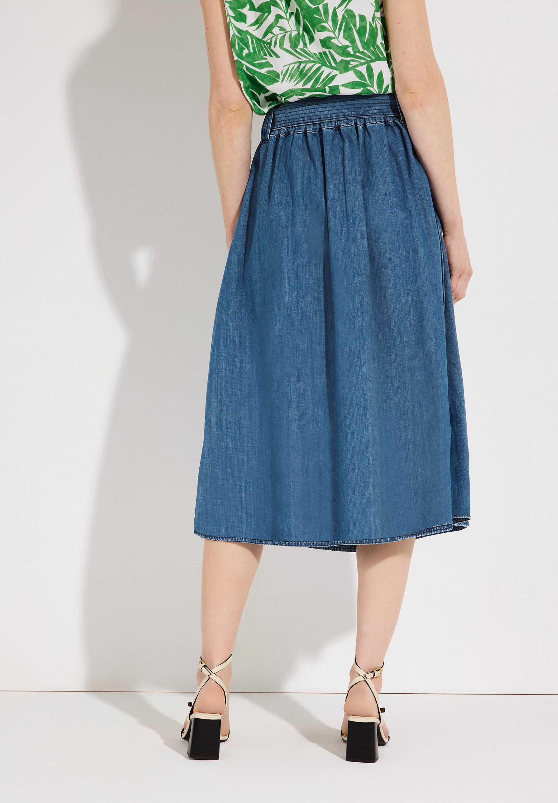 Eine Person trägt einen Jeansrock der Marke MORE & MORE und Sandalen mit Absatz. Eine Person trägt einen Jeansrock der Marke MORE & MORE und Sandalen mit Absatz.